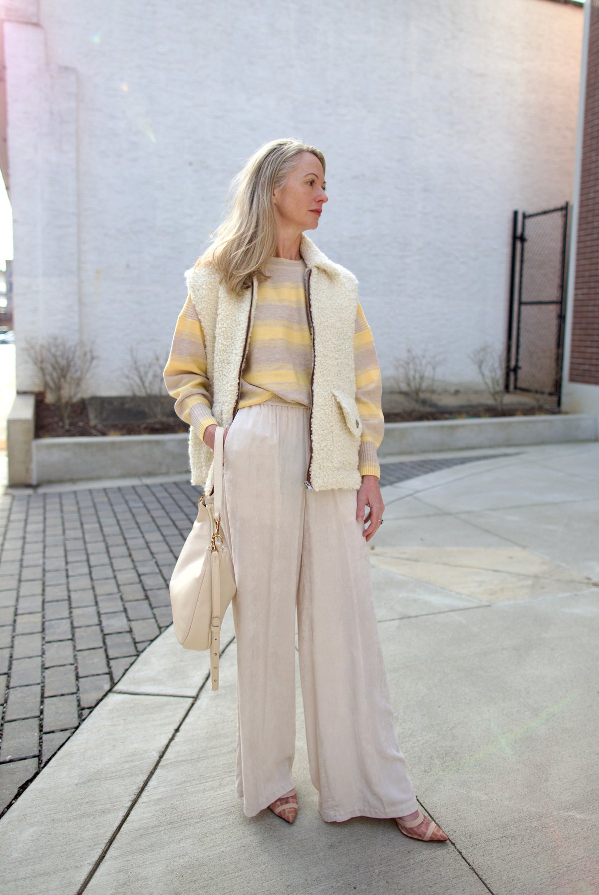 Mature woman holding Mansur Gavriel Swing leather bag in Ivory a warm winter white with two optional leather straps for a versitale handbag ready for any adventure