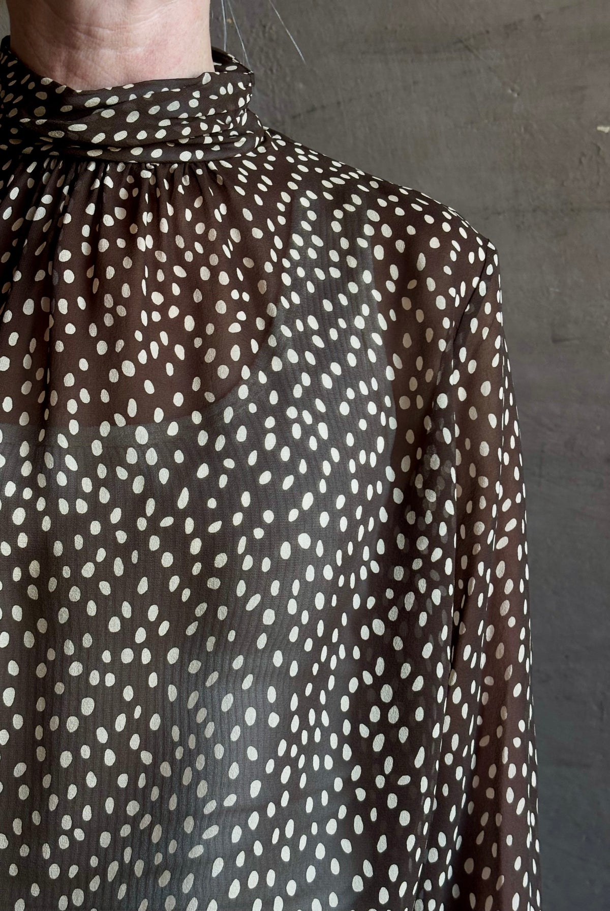 Mature woman wearing Nili Lotan Silk Demie Blouse in Brown/Cream Wild Dots sheer mock neck and keyhole back closure. Made in the USA