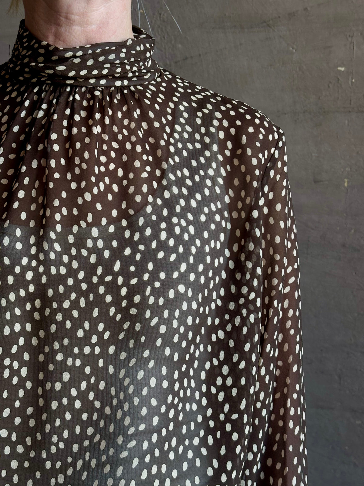 Mature woman wearing Nili Lotan Silk Demie Blouse in Brown/Cream Wild Dots sheer mock neck and keyhole back closure. Made in the USA
