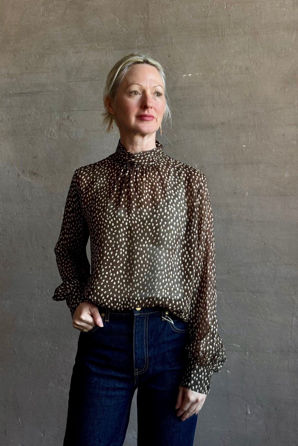 Mature woman wearing Nili Lotan Silk Demie Blouse in Brown/Cream Wild Dots sheer mock neck and keyhole back closure. Made in the USA