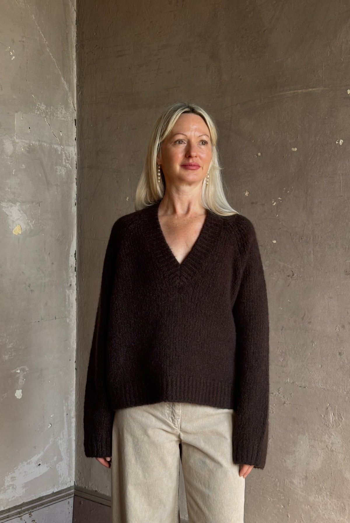 Mature woman wearing Nili Lotan's Isley Sweater Dark brown cashmere-silk relaxed V-neck silhouette. Ultra-luxe