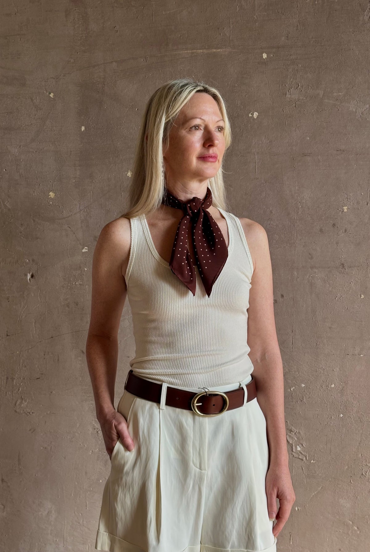 A mature woman wearing and brown scarf with small white polka-dot pattern as a neck tie