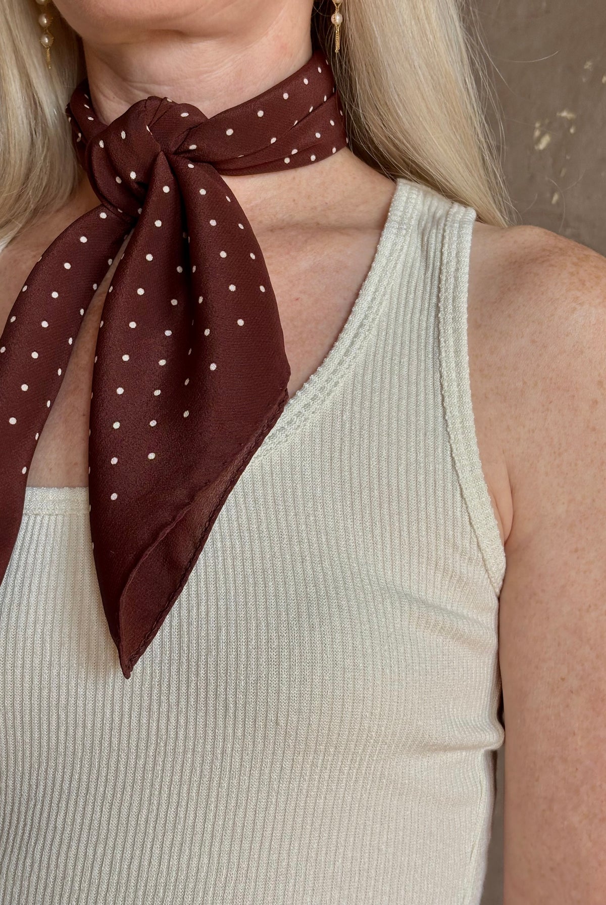 A mature woman wearing and brown scarf with small white polka-dot pattern as a neck tie