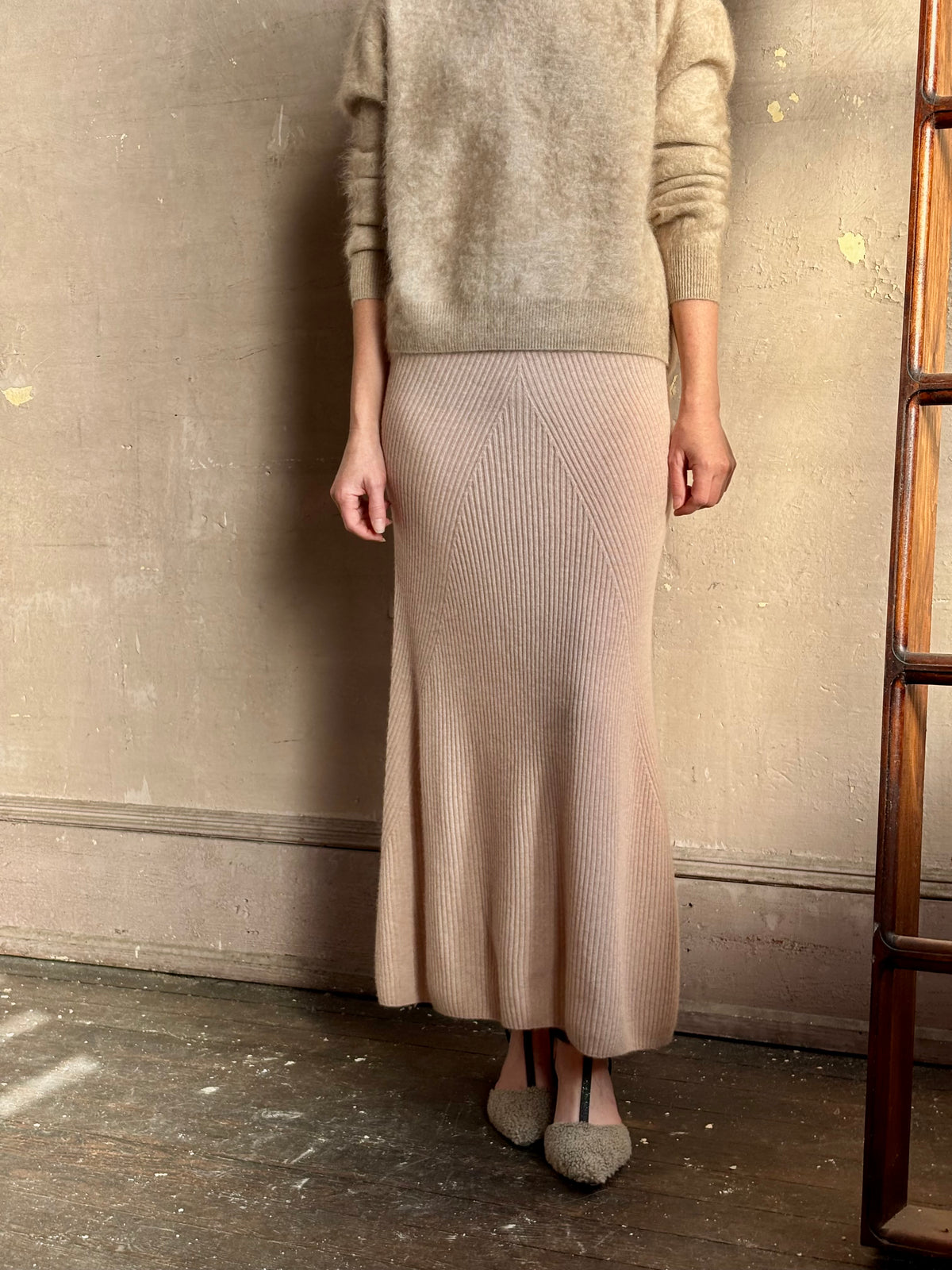 Close up image of a mature woman wearing Naadam's Ribbed Maxi Skirt in Blush with modern ribbed V pattern details in a flattering feminine silhouette
