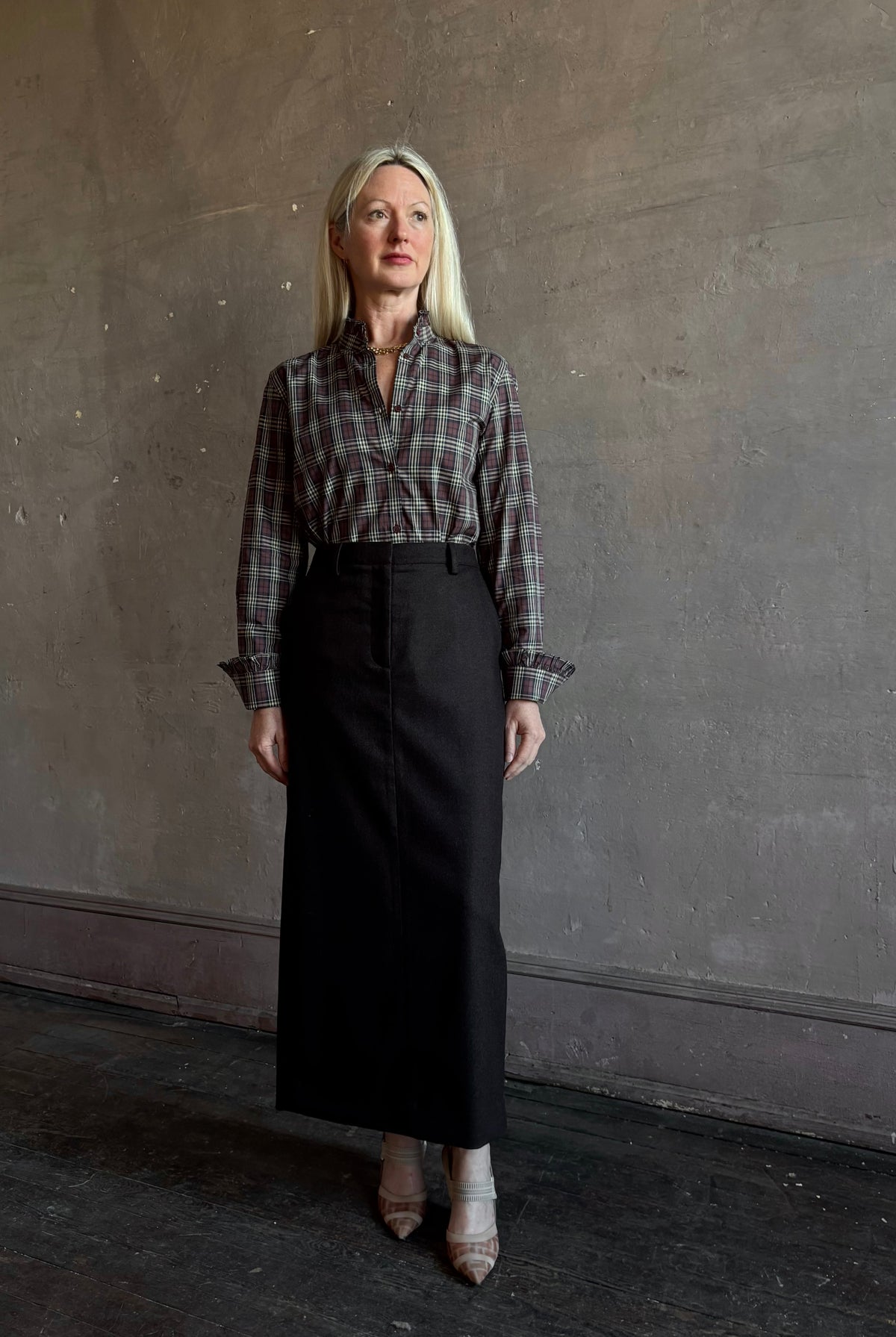 Mature woman wearing Nili Lotan’s Elio Shirt in burgundy and navy plaid print with ruffle-trimmed cuffs and collar tucked into a dark brown wool maxi pencil skirt for Fall