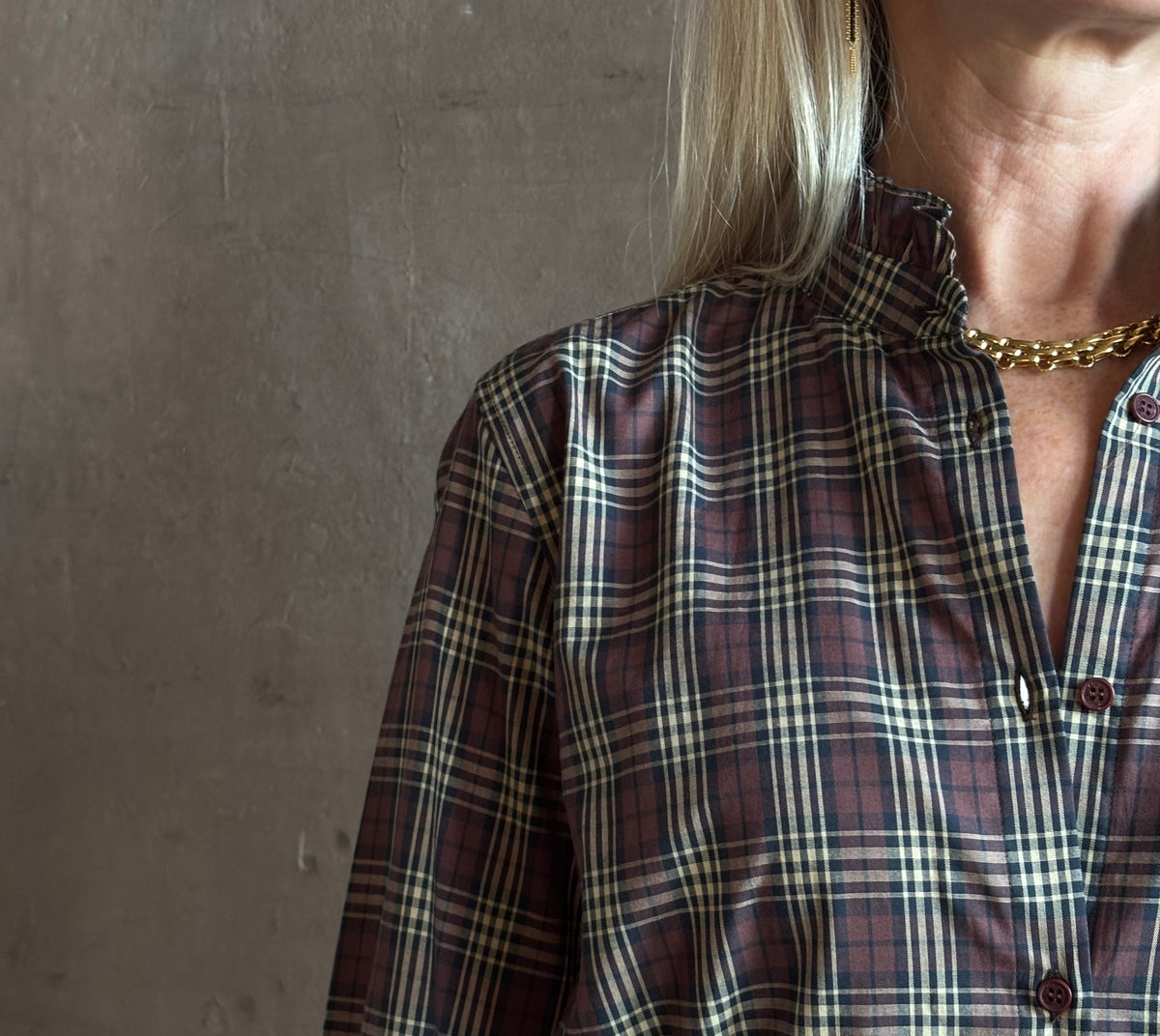 close-up image of a woman wearing a long-sleeve plaid button-up shirt in dark red, beige, and navy by Nili Lotan in Elio Ruffle collar feminine sihlouette