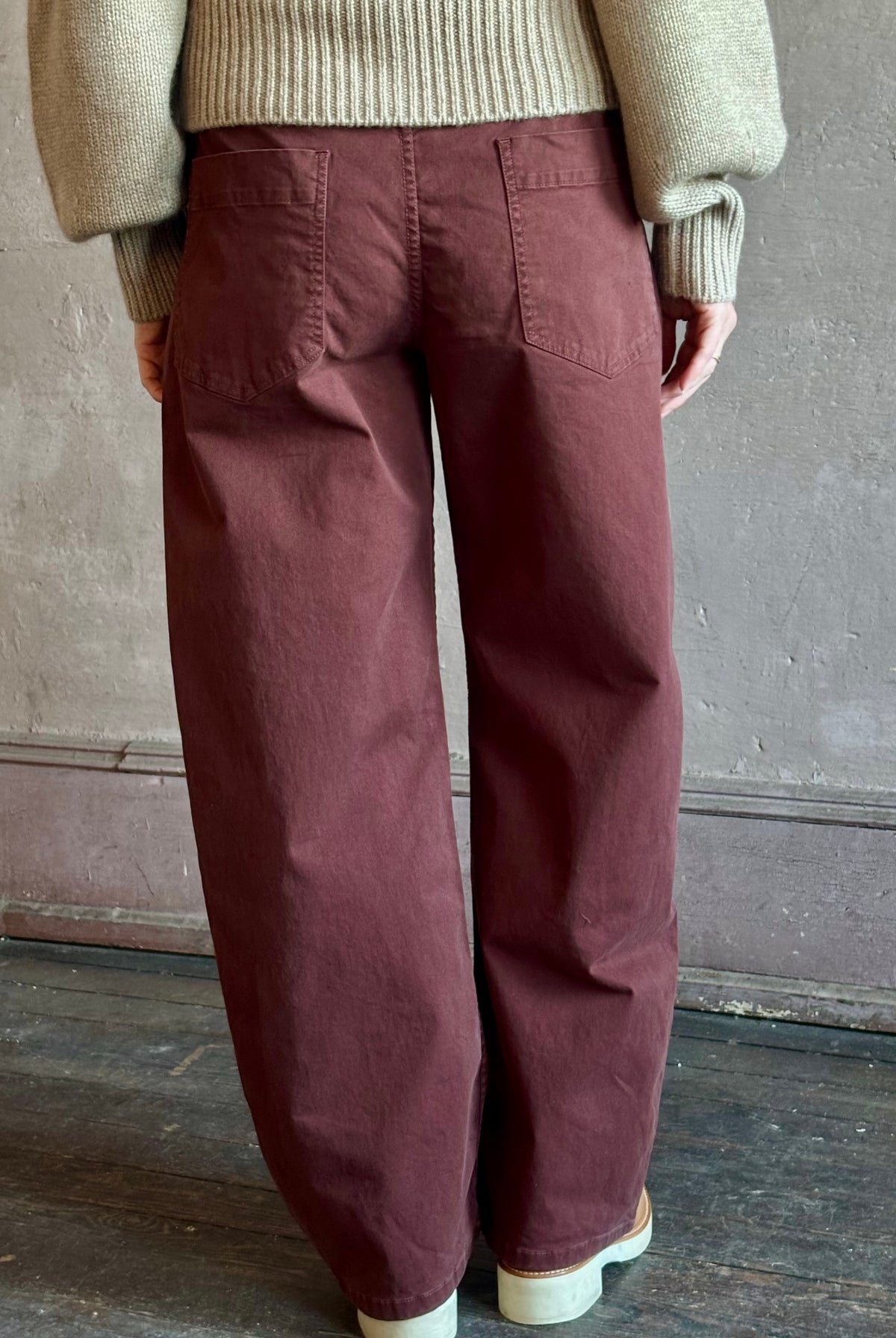 Back view of woman wearing Nili Lotan’s Tribeca Pant in a cotton-elastane barrel leg relaxed fit back patch pockets in burgundy Made in the USA