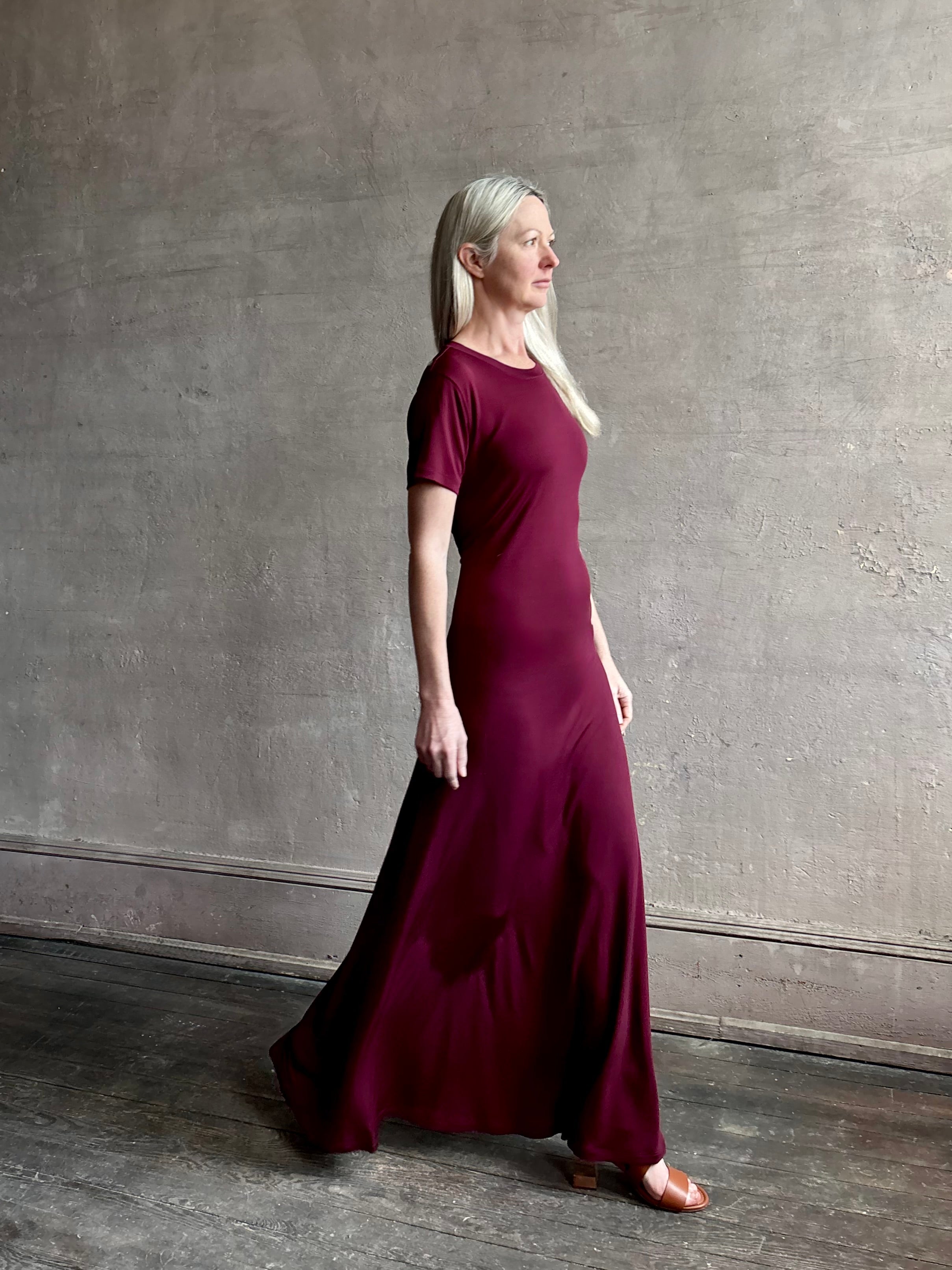 Mature woman wearing the Noelle designer dress from Proenza Schouler in a deep wine hue with elevated back draping detail short sleeves and crew neck