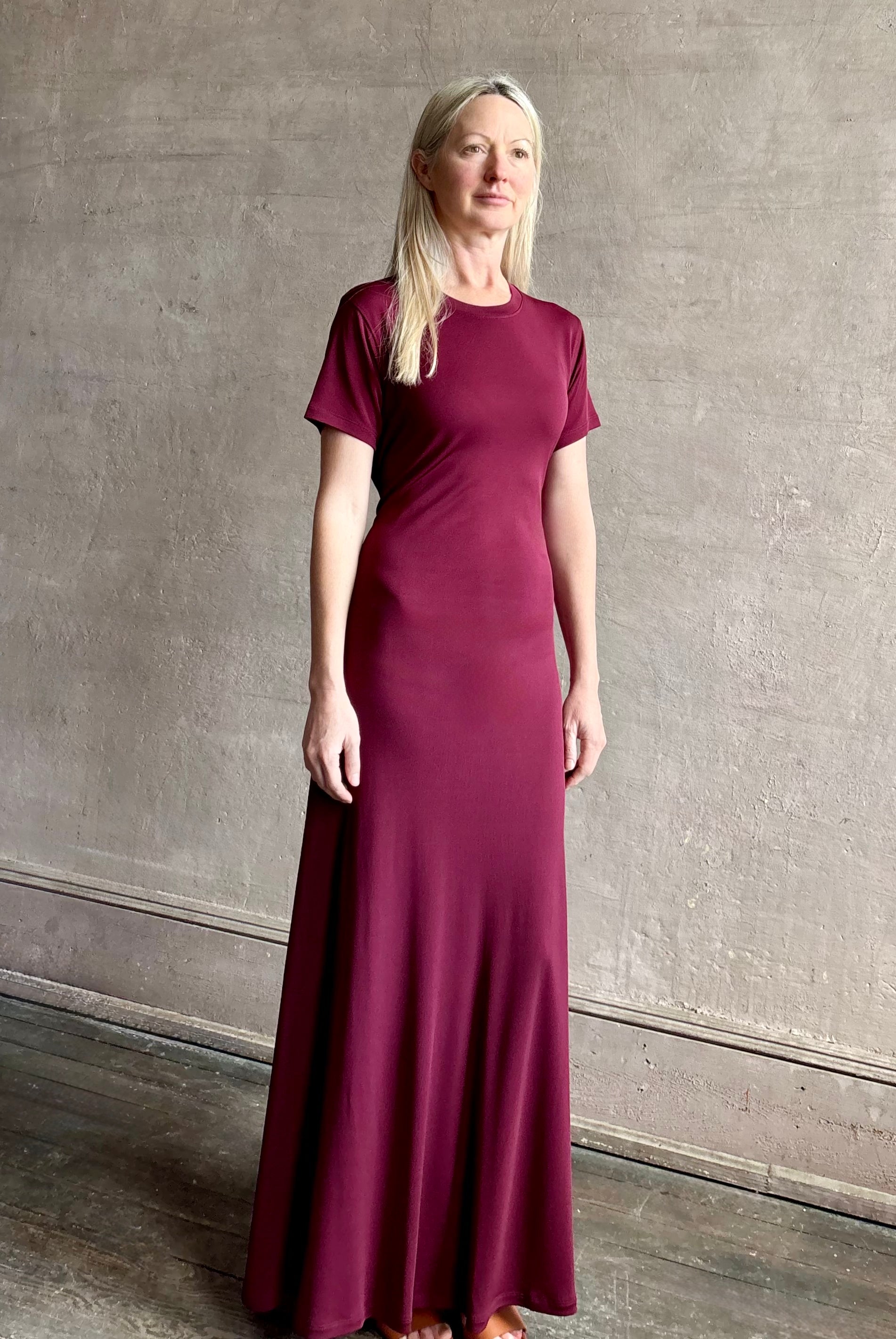 Mature woman wearing the Noelle designer dress from Proenza Schouler in a deep wine hue with elevated back draping detail short sleeves and crew neck