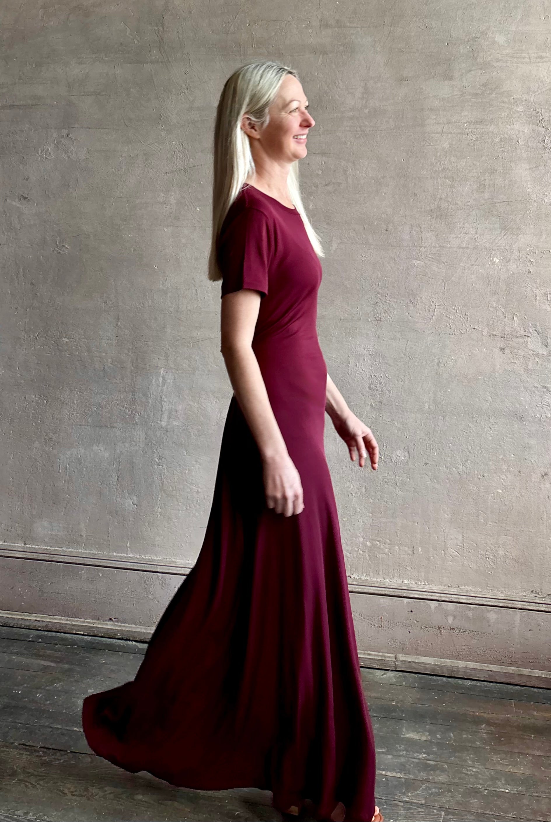 Mature woman wearing the Noelle designer dress from Proenza Schouler in a deep wine hue with elevated back draping detail short sleeves and crew neck