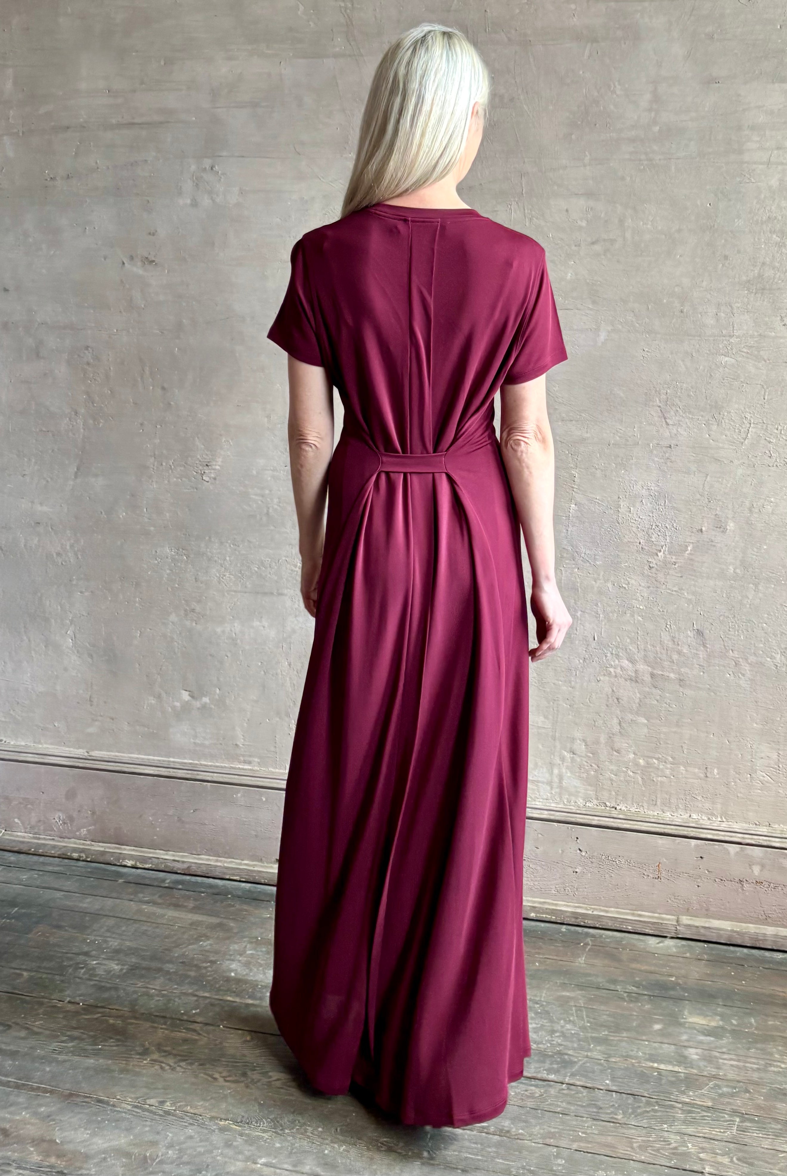 Mature woman wearing the Noelle designer dress from Proenza Schouler in a deep wine hue with elevated back draping detail short sleeves and crew neck