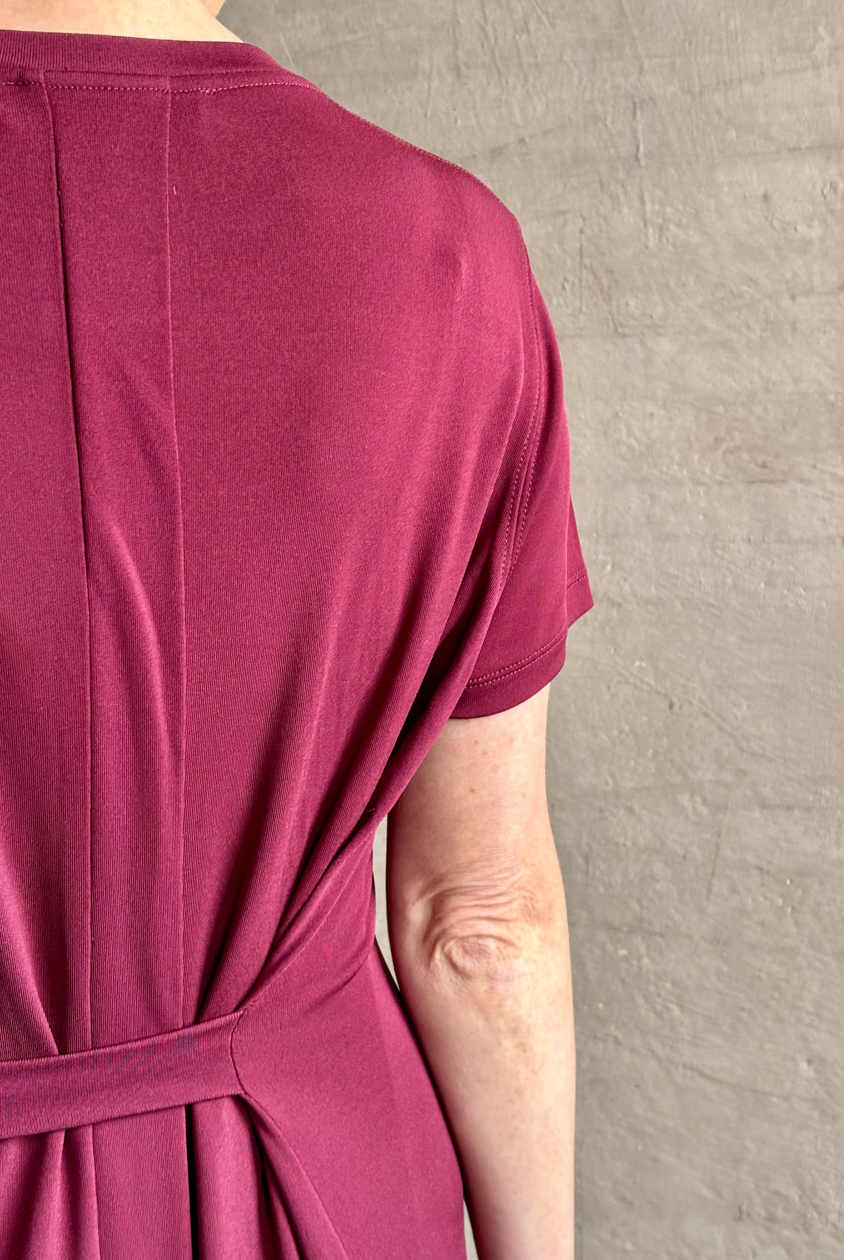 Mature woman wearing the Noelle designer dress from Proenza Schouler in a deep wine hue with elevated back draping detail short sleeves and crew neck