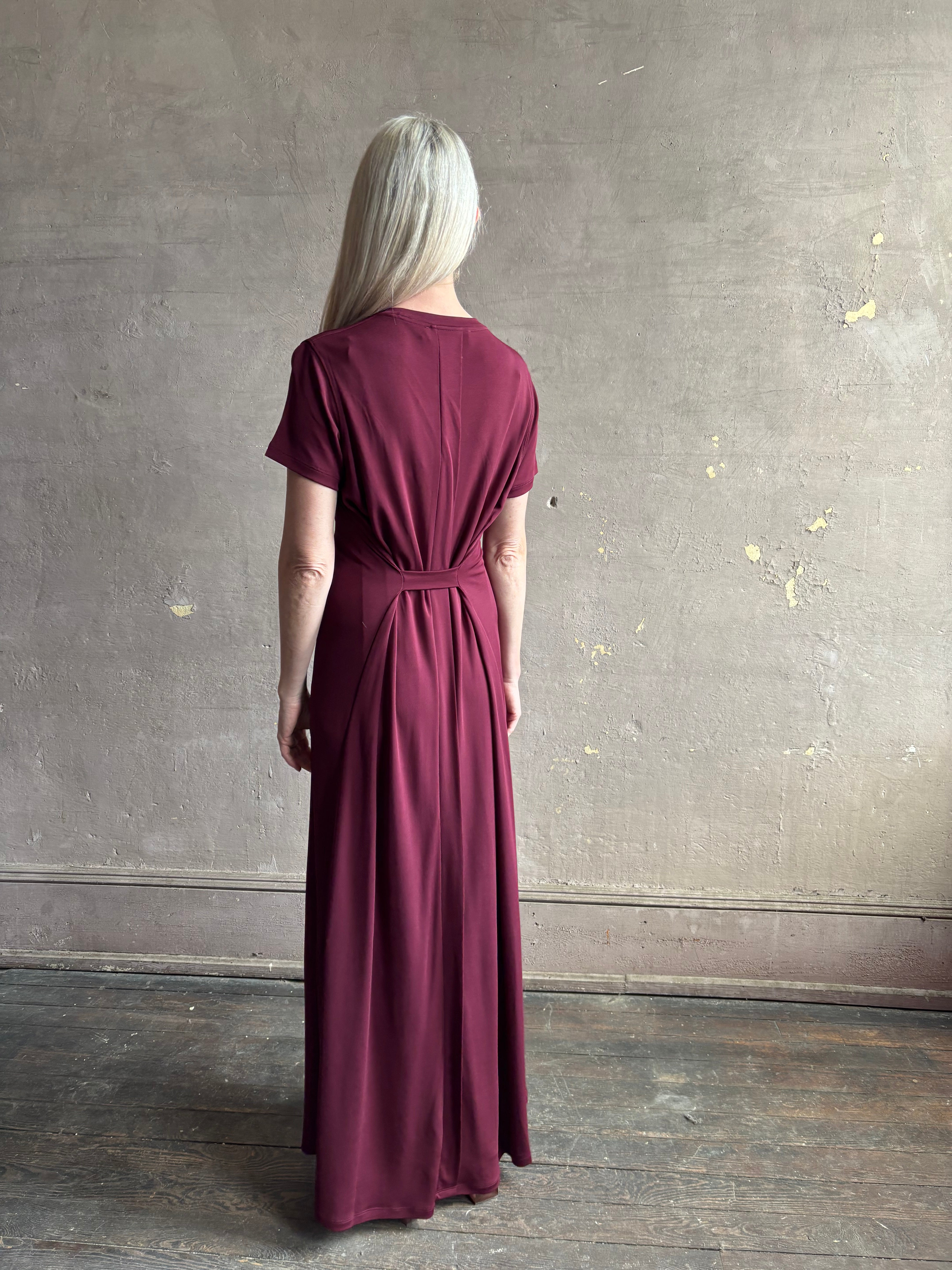 Mature woman wearing the Noelle designer dress from Proenza Schouler in a deep wine hue with elevated back draping detail short sleeves and crew neck