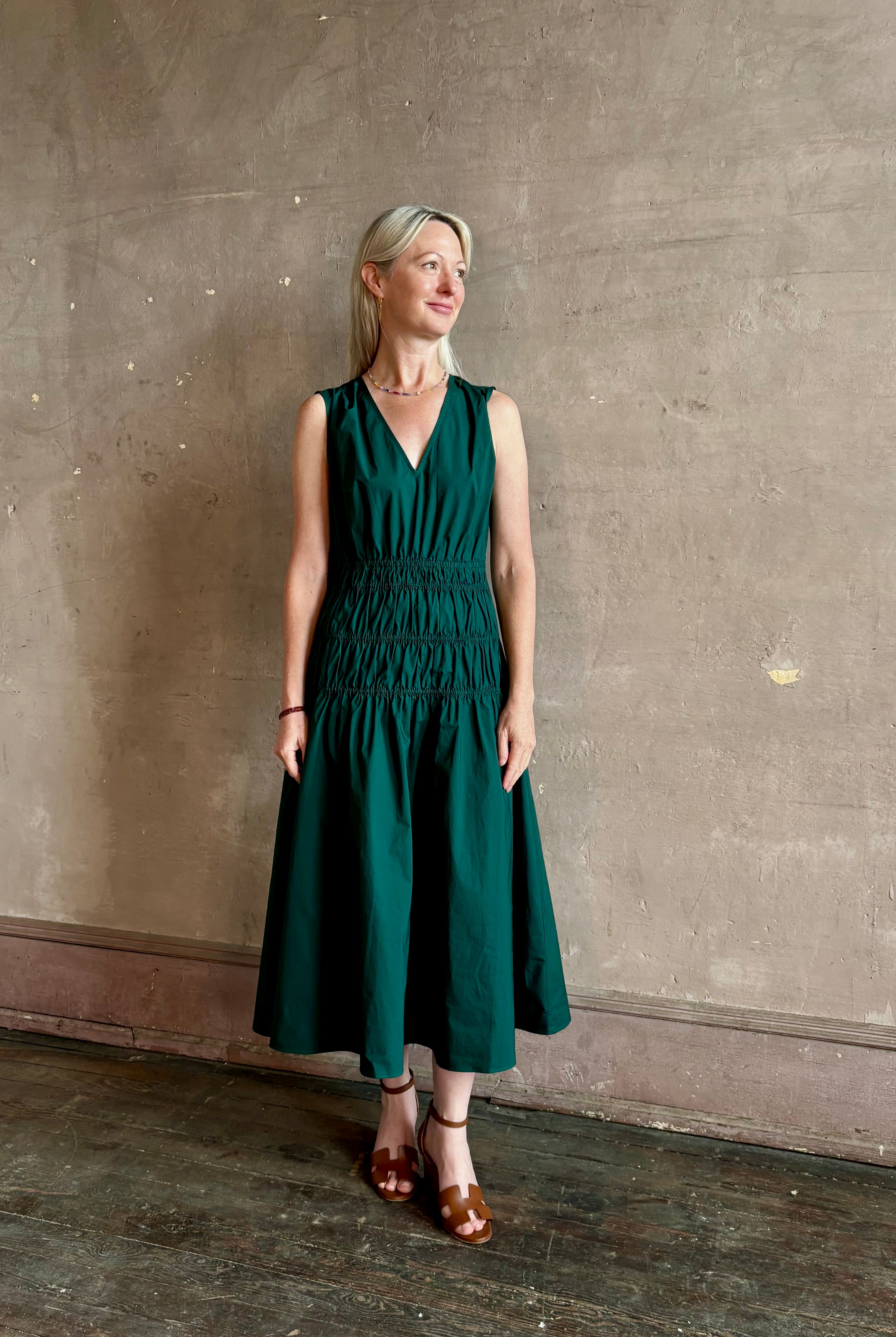 Mature woman wearing Loren Dress from Proenza Schouler White Lable rendered in aspruce green and crafted from a cotton elastane blend with v-neck, sleeveless, pockets, and rushed waist