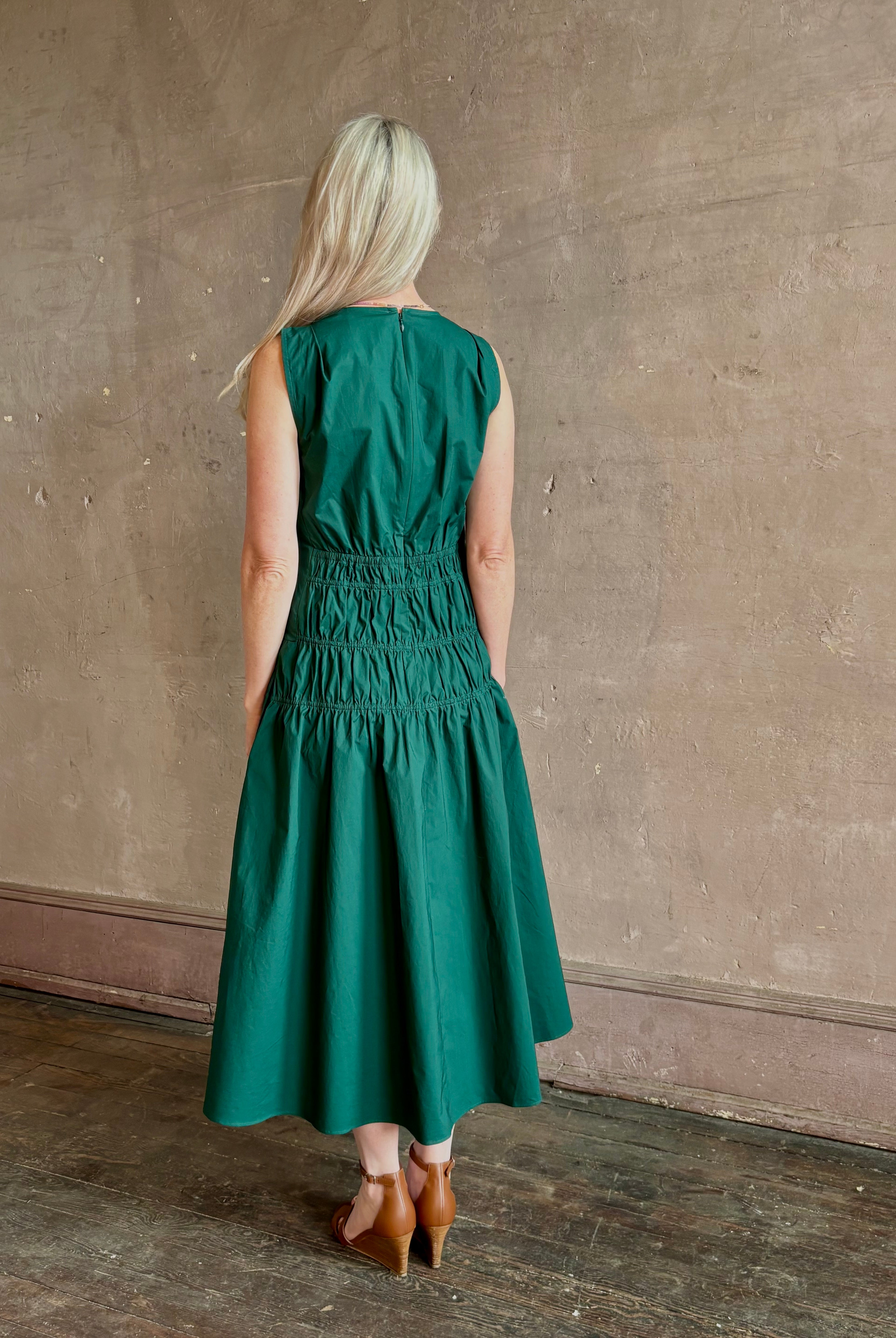 Mature woman wearing Loren Dress from Proenza Schouler White Lable rendered in aspruce green and crafted from a cotton elastane blend with v-neck, sleeveless, pockets, and rushed waist