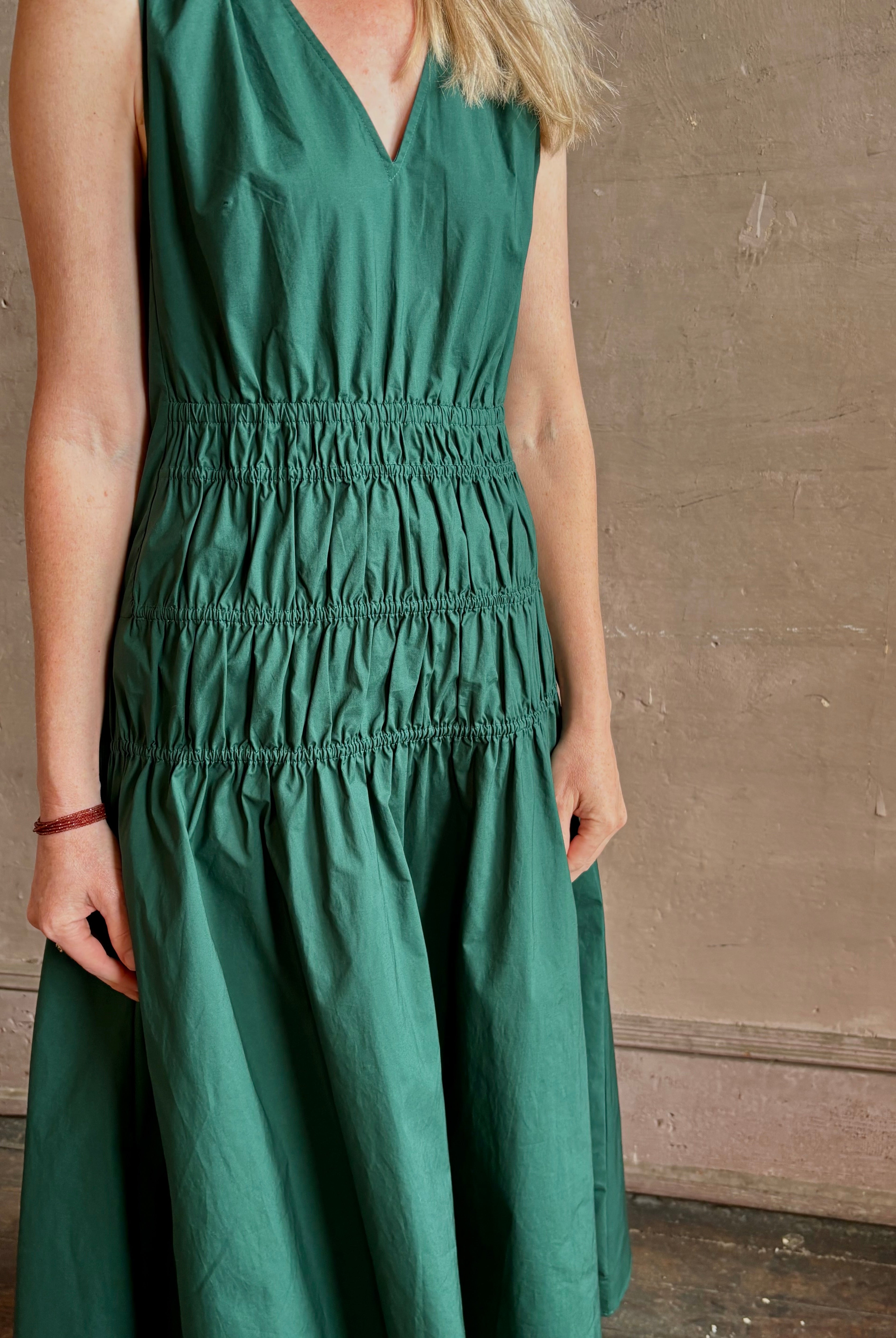 Mature woman wearing Loren Dress from Proenza Schouler White Lable rendered in aspruce green and crafted from a cotton elastane blend with v-neck, sleeveless, pockets, and rushed waist
