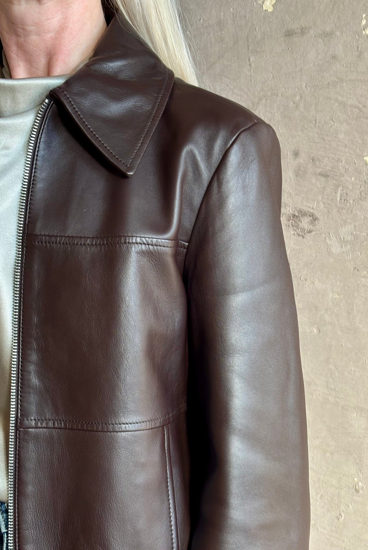 Close up image of mature woman wearing Proenza Schouler White Label Annabel Leather Jacket in Chocolate Brown with intricate seam details on front of jacket that wrap around the back