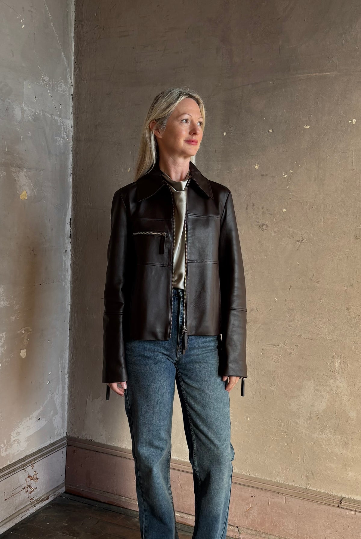 Mature woman wearing Proenza Schouler White Label Annabel lambskin Leather biker Jacket in Chocolate Brown with two way front zipper and straight hem