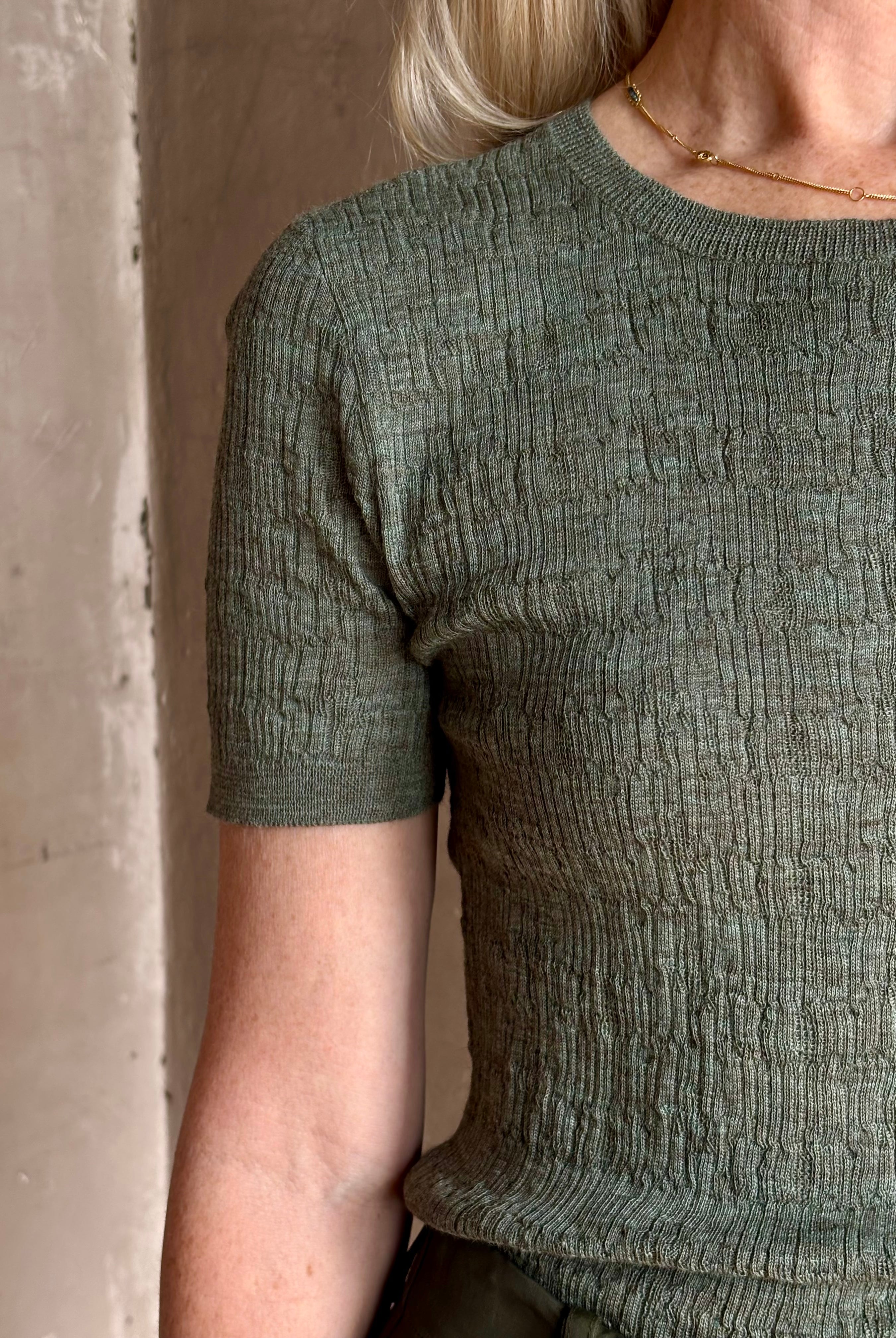 Mature woman wearing a textured short-sleeve fitted knit top in sage green round neckline with brown heathering
