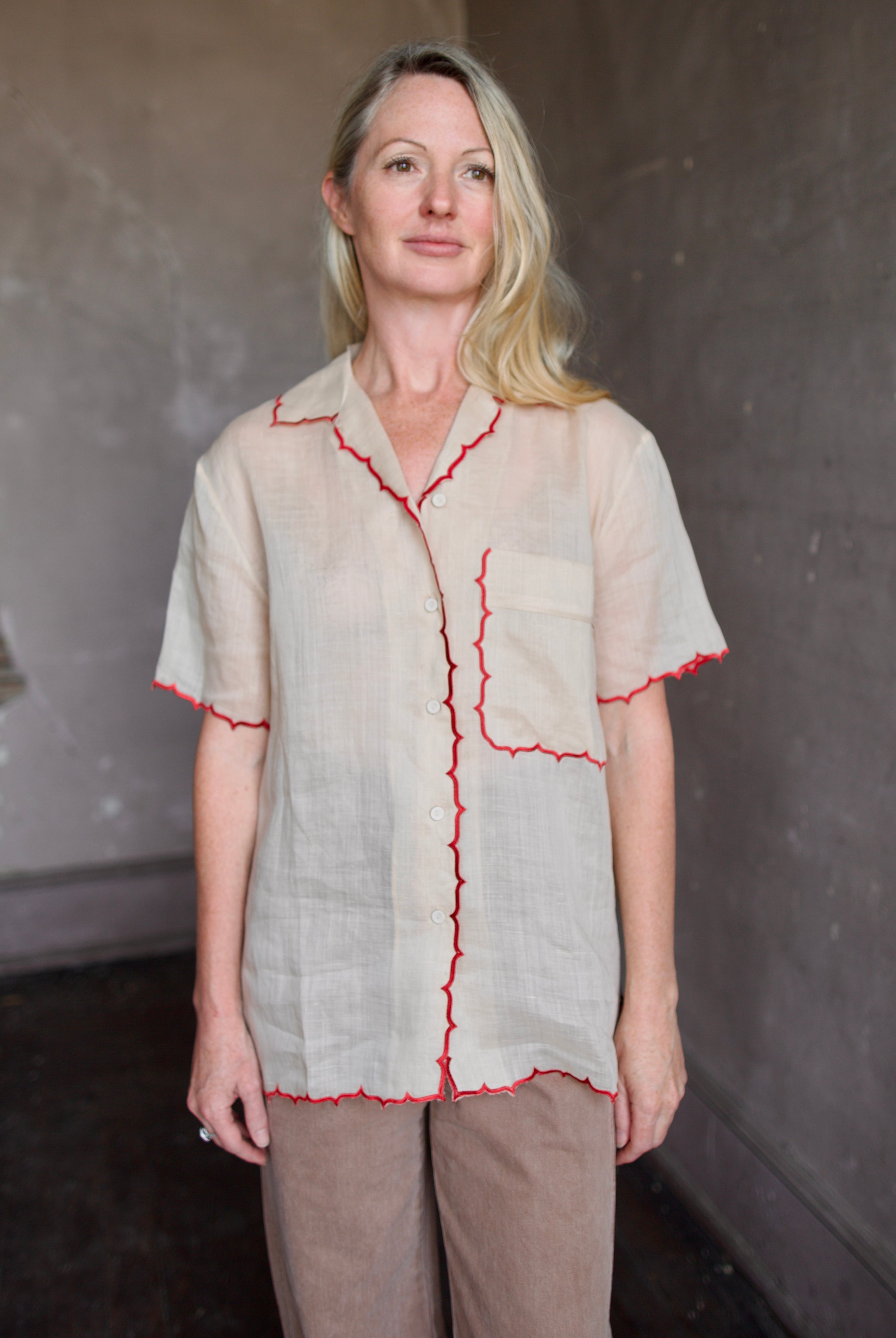 Model wearing a beige retro inspired blouse with scalloped red trim by Rachel Comey in raimey