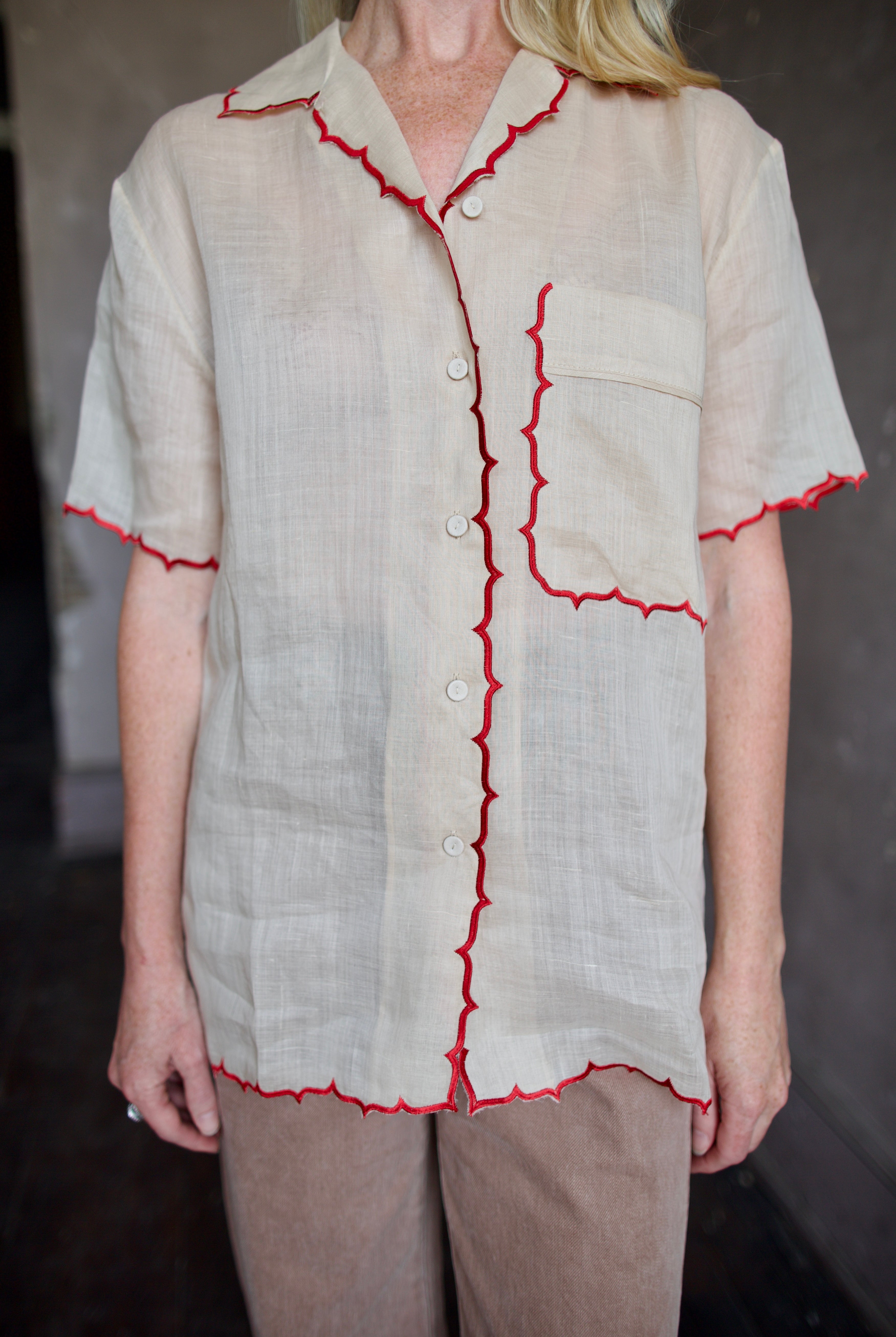 Model wearing a beige retro inspired blouse with scalloped red trim by Rachel Comey in raimey