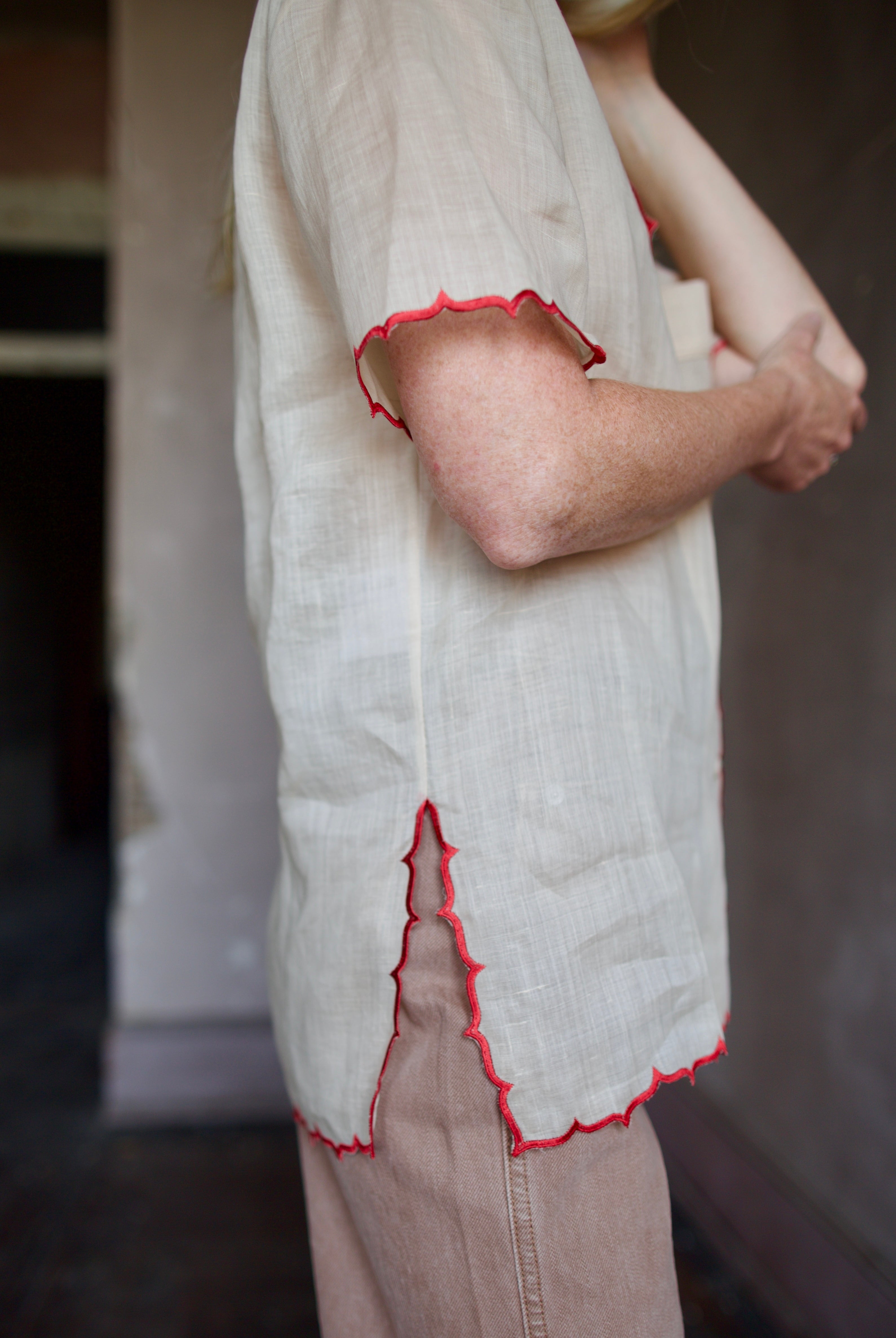 Model wearing a beige retro inspired blouse with scalloped red trim by Rachel Comey in raimey