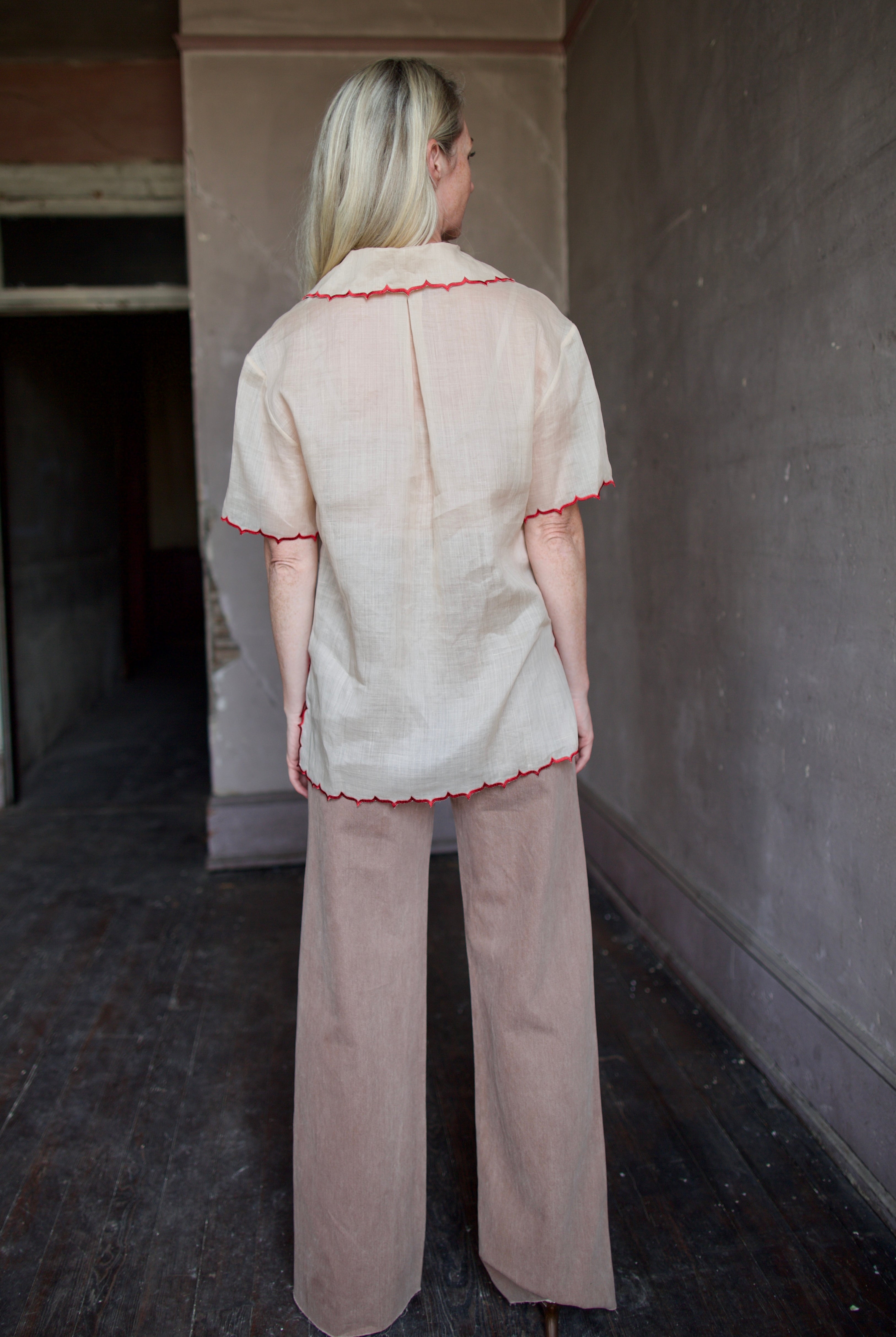 Model wearing a beige retro inspired blouse with scalloped red trim by Rachel Comey in raimey