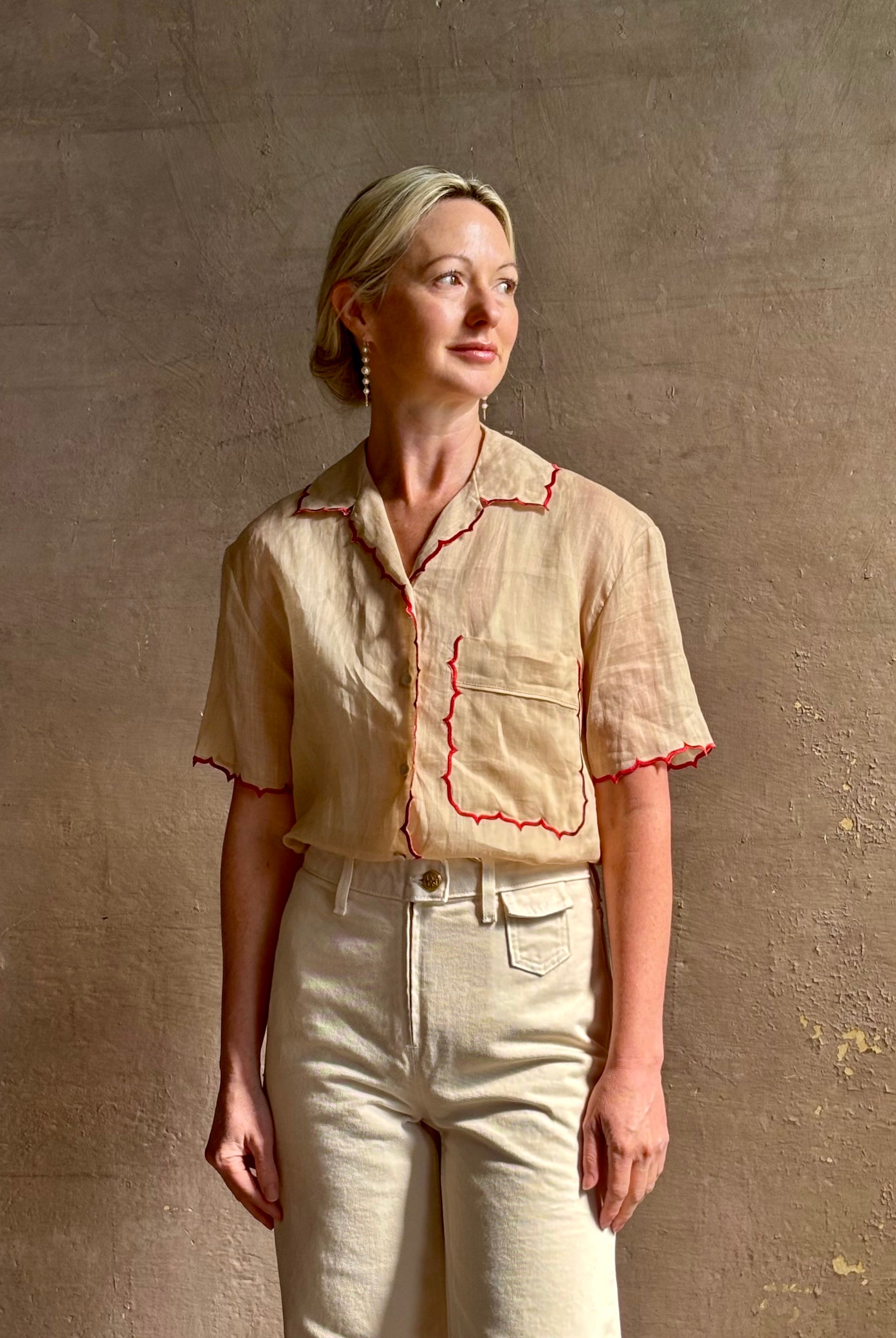 Mature woman wearing a beige retro inspired blouse with scalloped red trim by New York based Women's clothing designer Rachel Comey in raimey