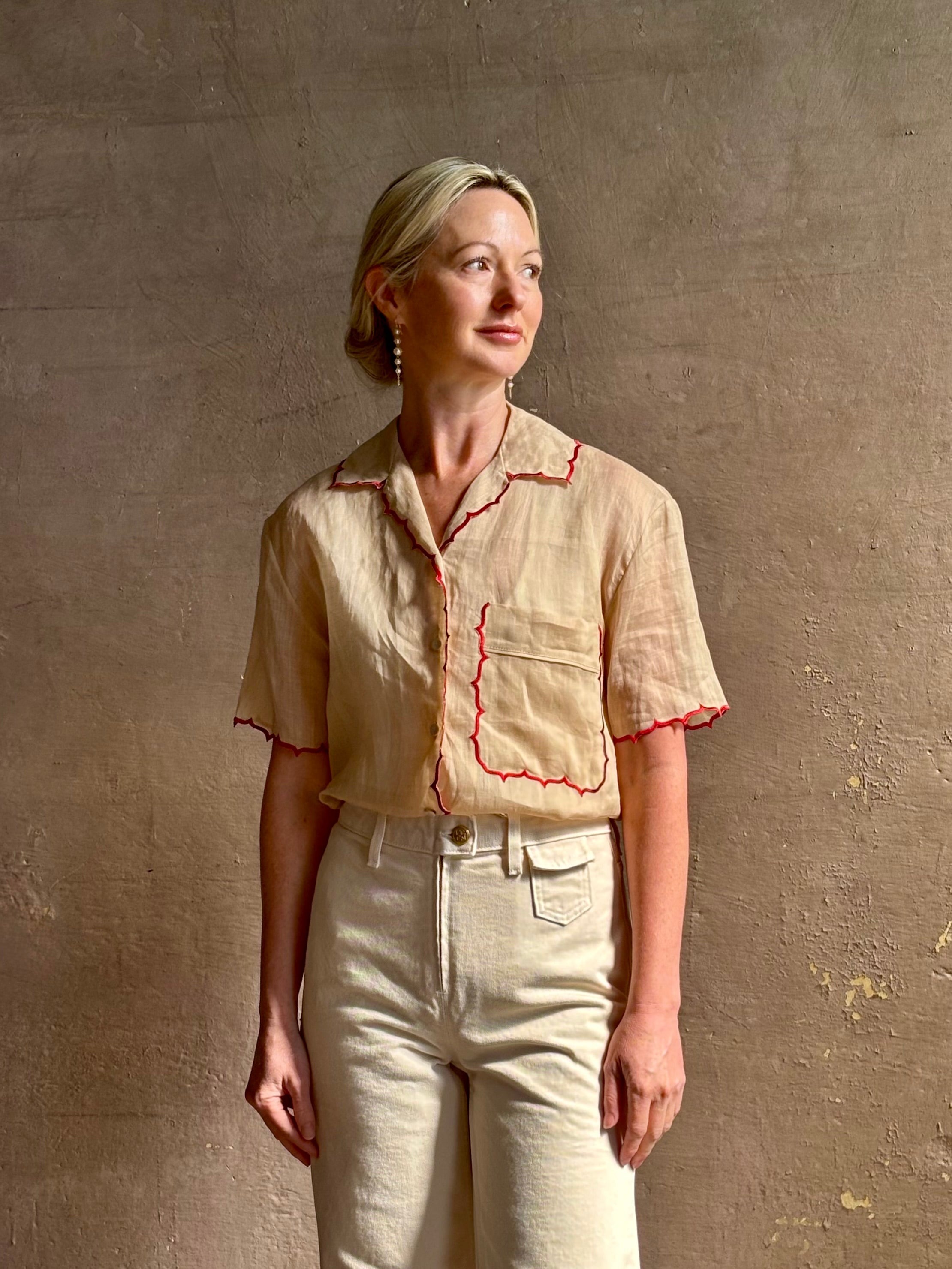 Mature woman wearing a beige retro inspired blouse with scalloped red trim by New York based Women's clothing designer Rachel Comey in raimey