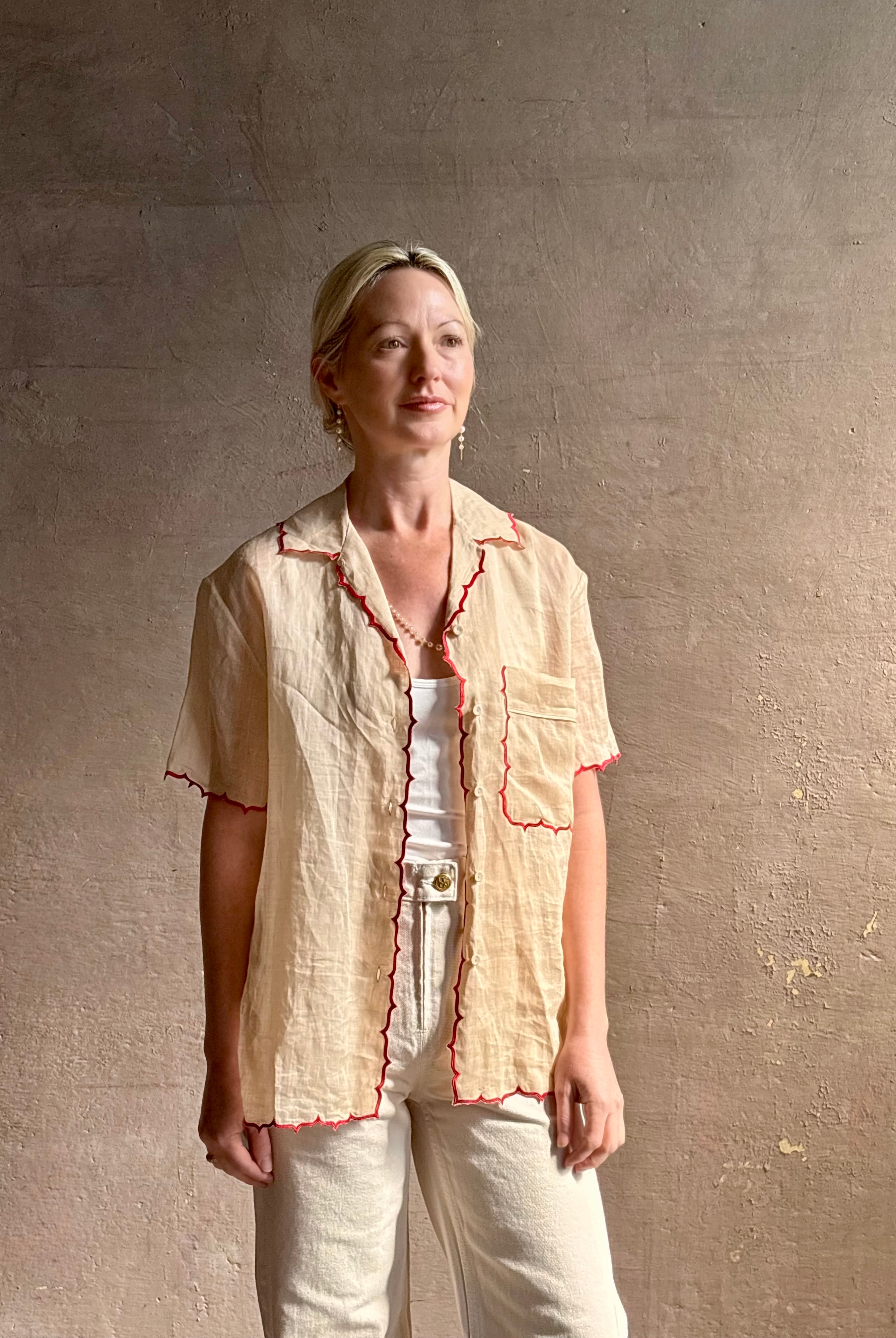 Mature woman wearing a beige retro inspired blouse with scalloped red trim by New York based Women's clothing designer Rachel Comey in raimey