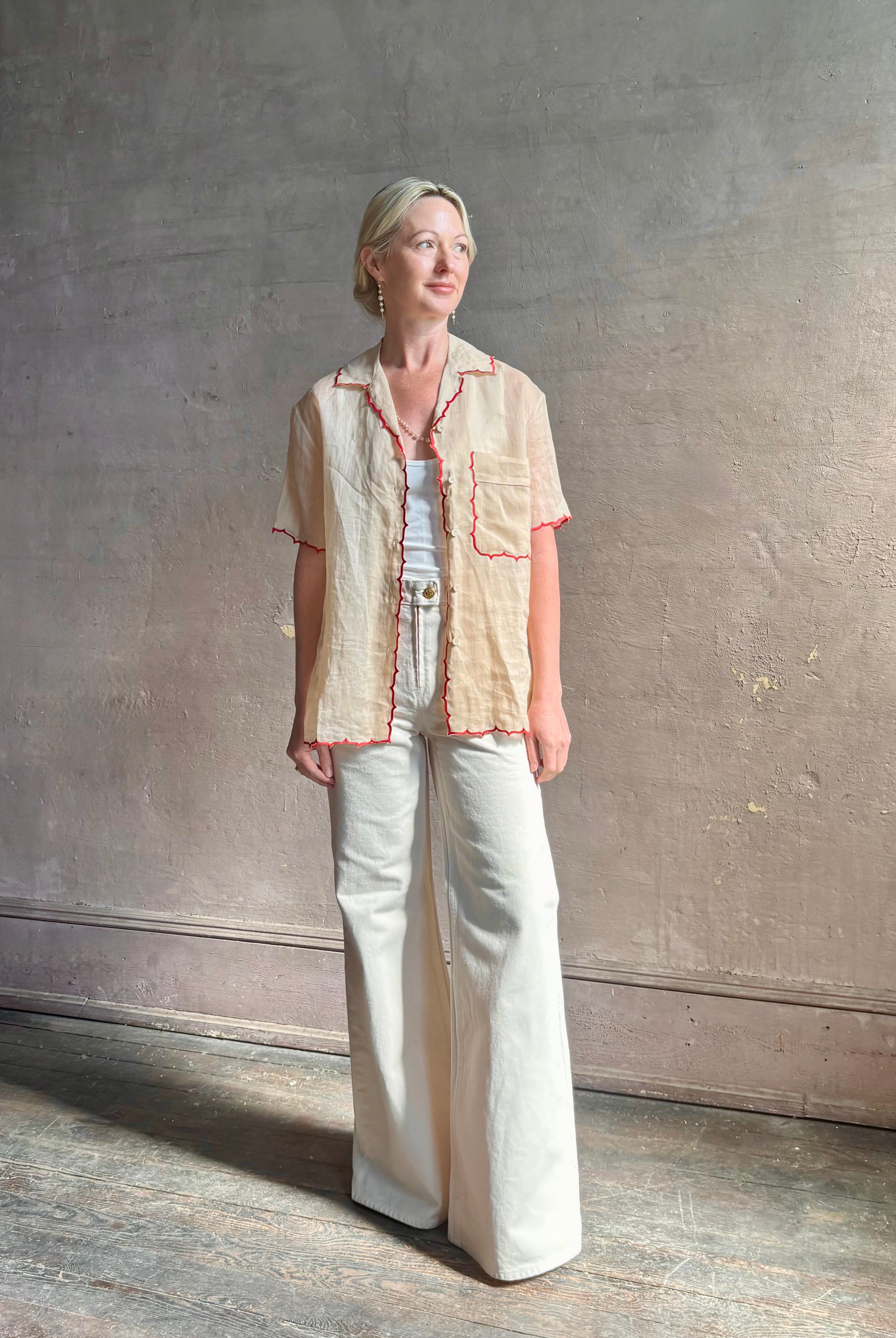 Mature woman wearing a beige retro inspired blouse with scalloped red trim by New York based Women's clothing designer Rachel Comey in raimey
