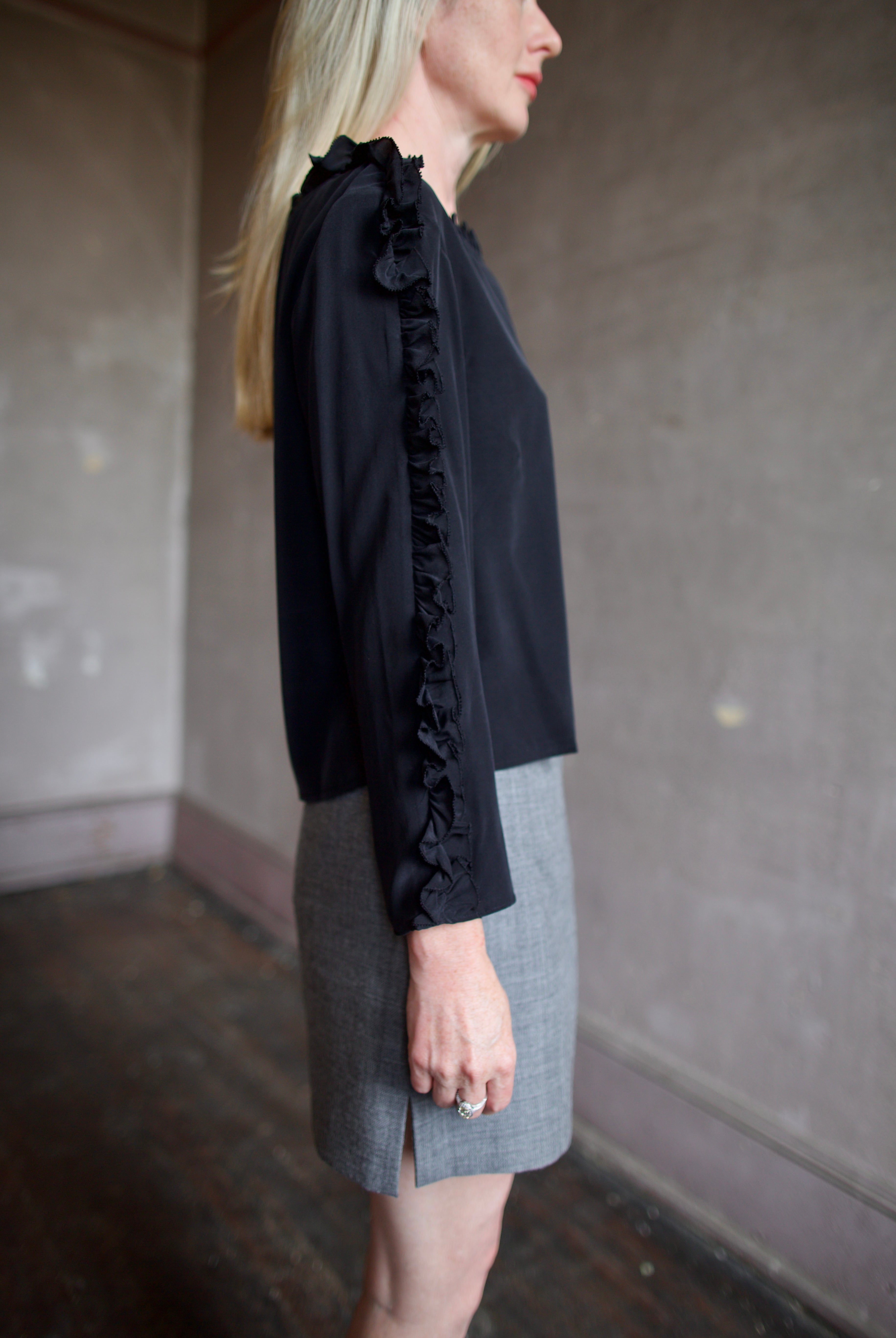 Mature model wearing a Rachel Comey black blouse with ruffled trim and an Apiece Apart gray wool skirt