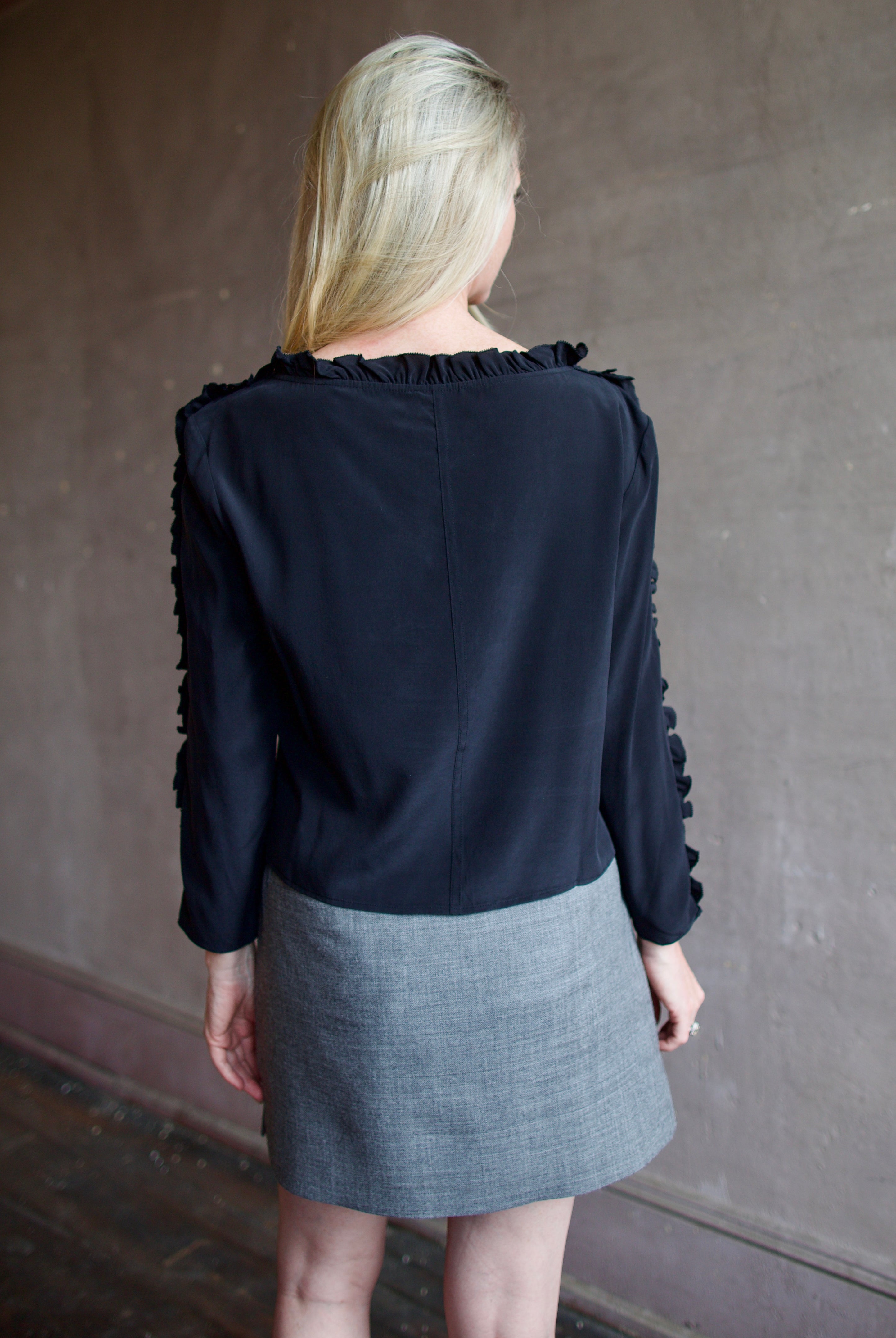 Mature model wearing a Rachel Comey black blouse with ruffled trim and an Apiece Apart gray wool skirt
