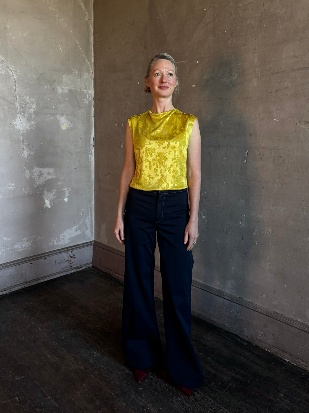 Mature woman wearing Rachel Comey Primula Pique Knit Top in Mustard yellow waterfall front tone-on-tone jacquard floral made in the USA