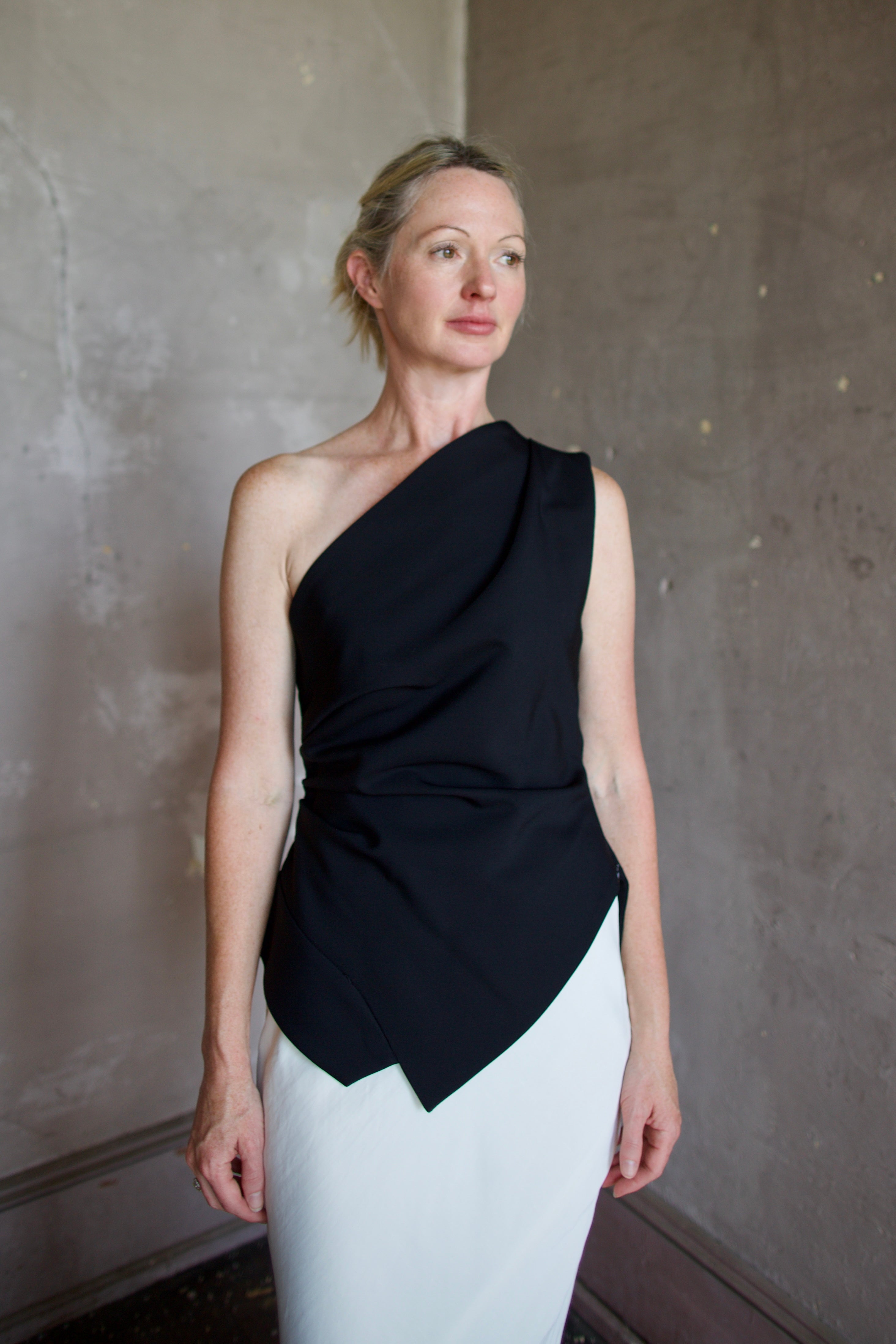 Model wearing sophisticated luxury modern designer brand Rohe flattering off shoulder lapel top in black