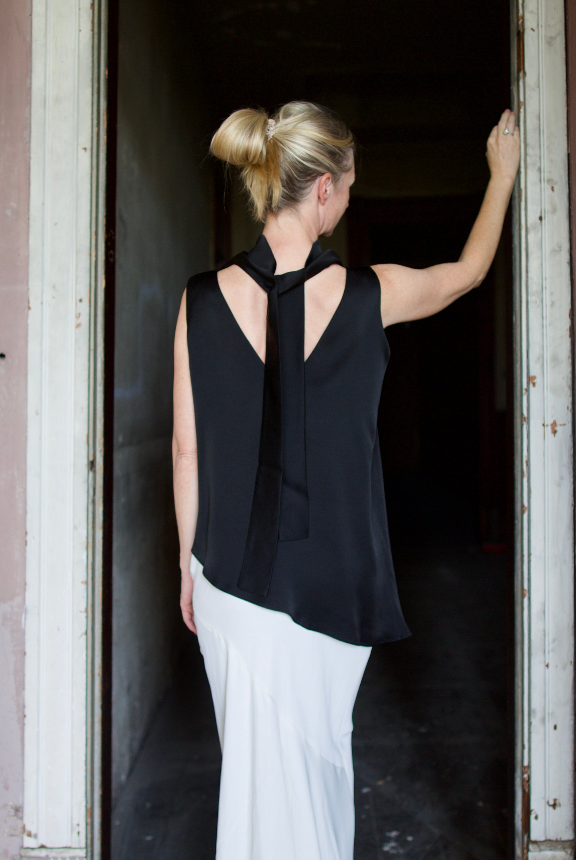 Model wearing black sleeveless satin top with expertly crafted draping and attached tie by luxury modern designer Rohe