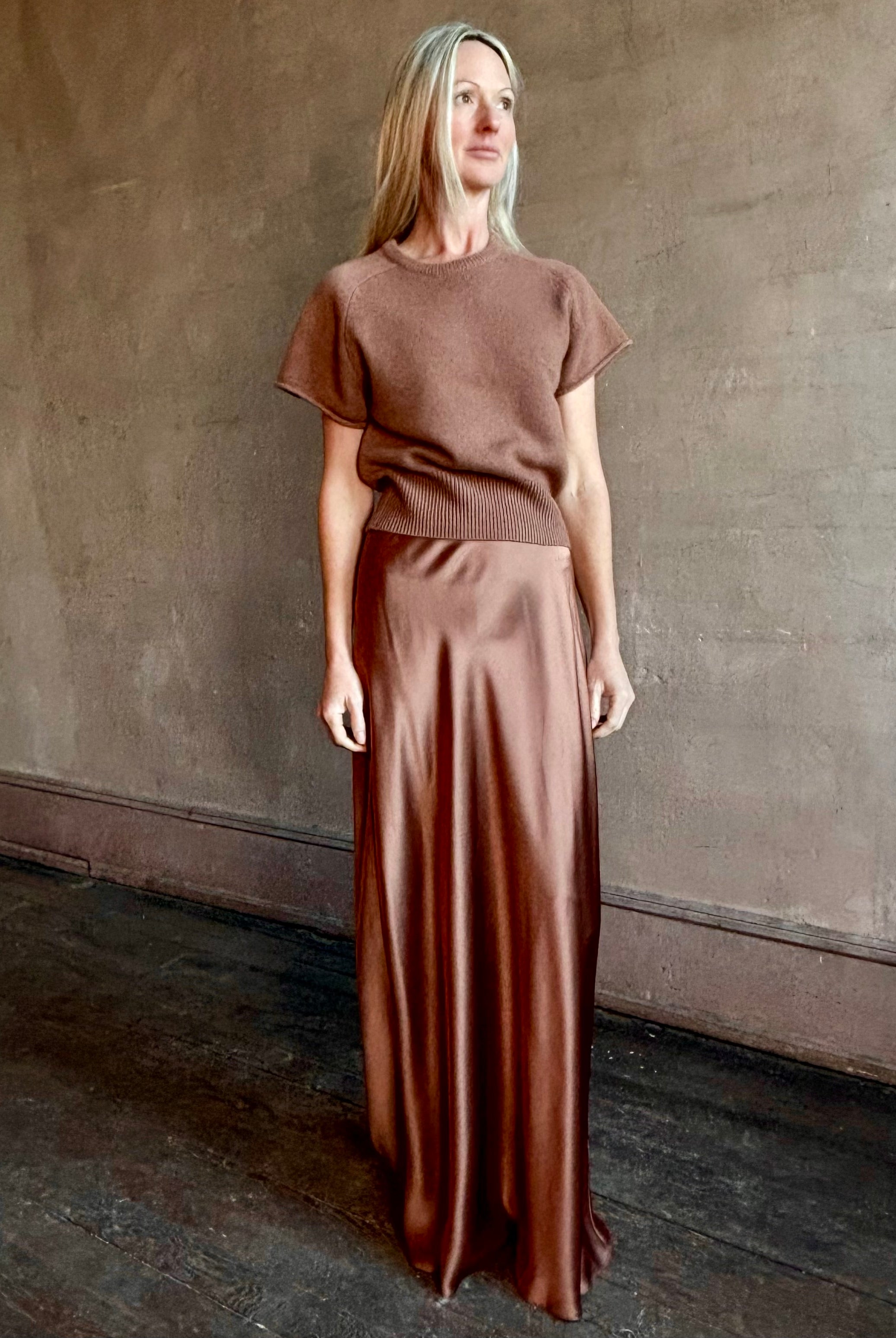 Woman wearing luxury SABLYN Grace Scallop Trim Bias Cut silk Maxi Pull On Skirt in a neutral copper color with matching sweater set