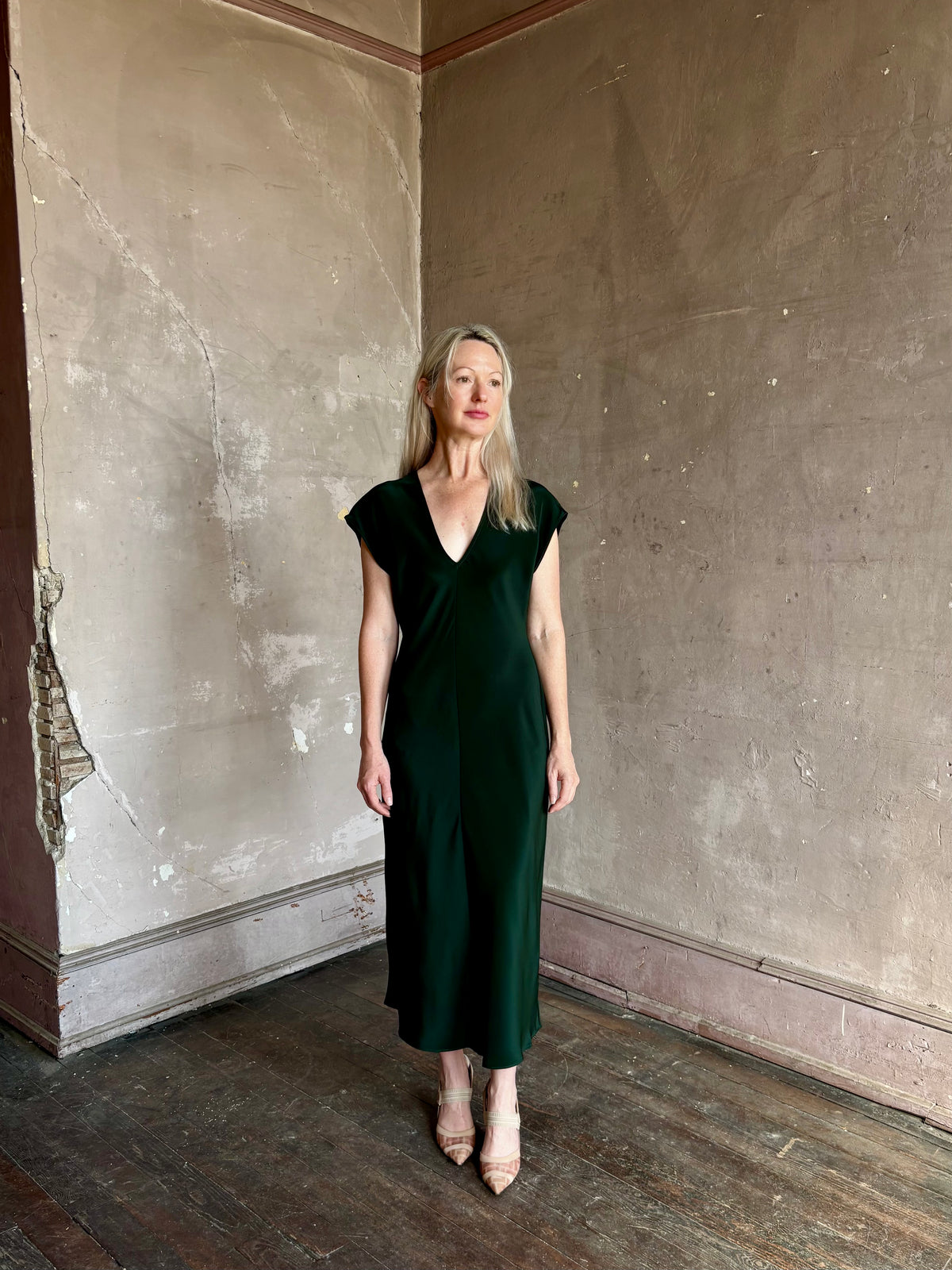 Mature woman wearing Sablyn Inez draped silk V-neck dark green midi dress with short cap sleeves made in USA