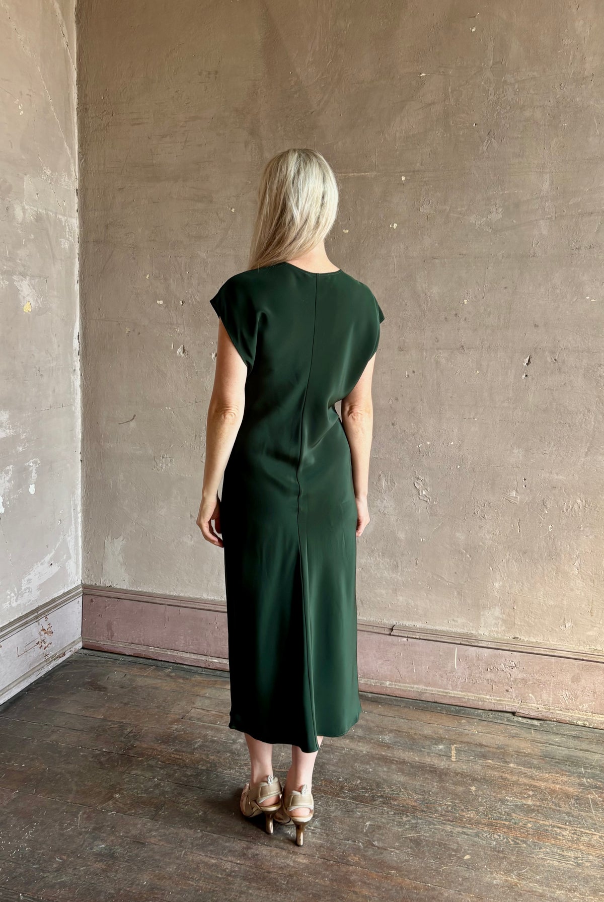 Mature woman wearing Sablyn Inez draped silk V-neck dark green midi dress with short cap sleeves made in USA