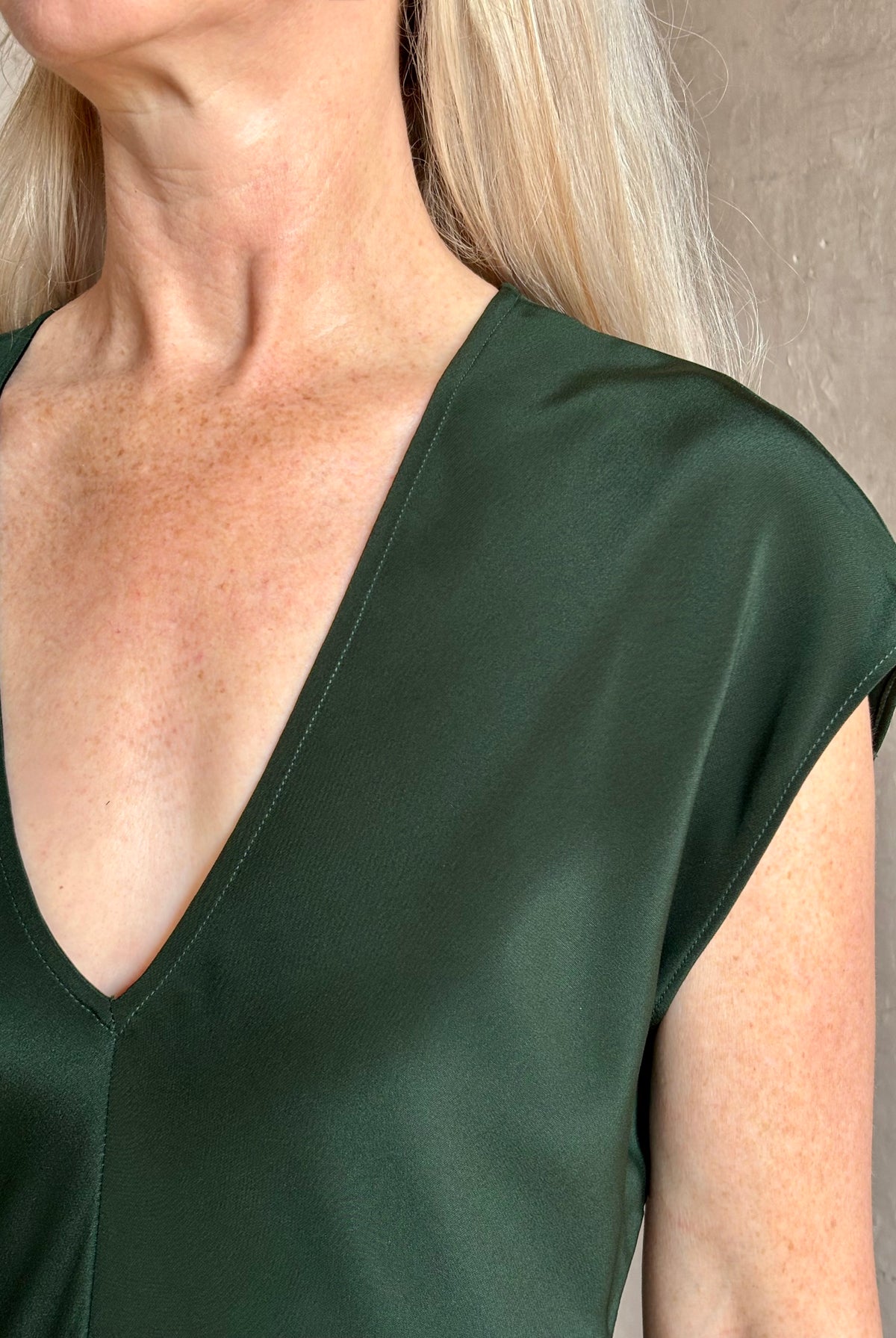 Mature woman wearing Sablyn Inez draped silk V-neck dark green midi dress with short cap sleeves made in USA