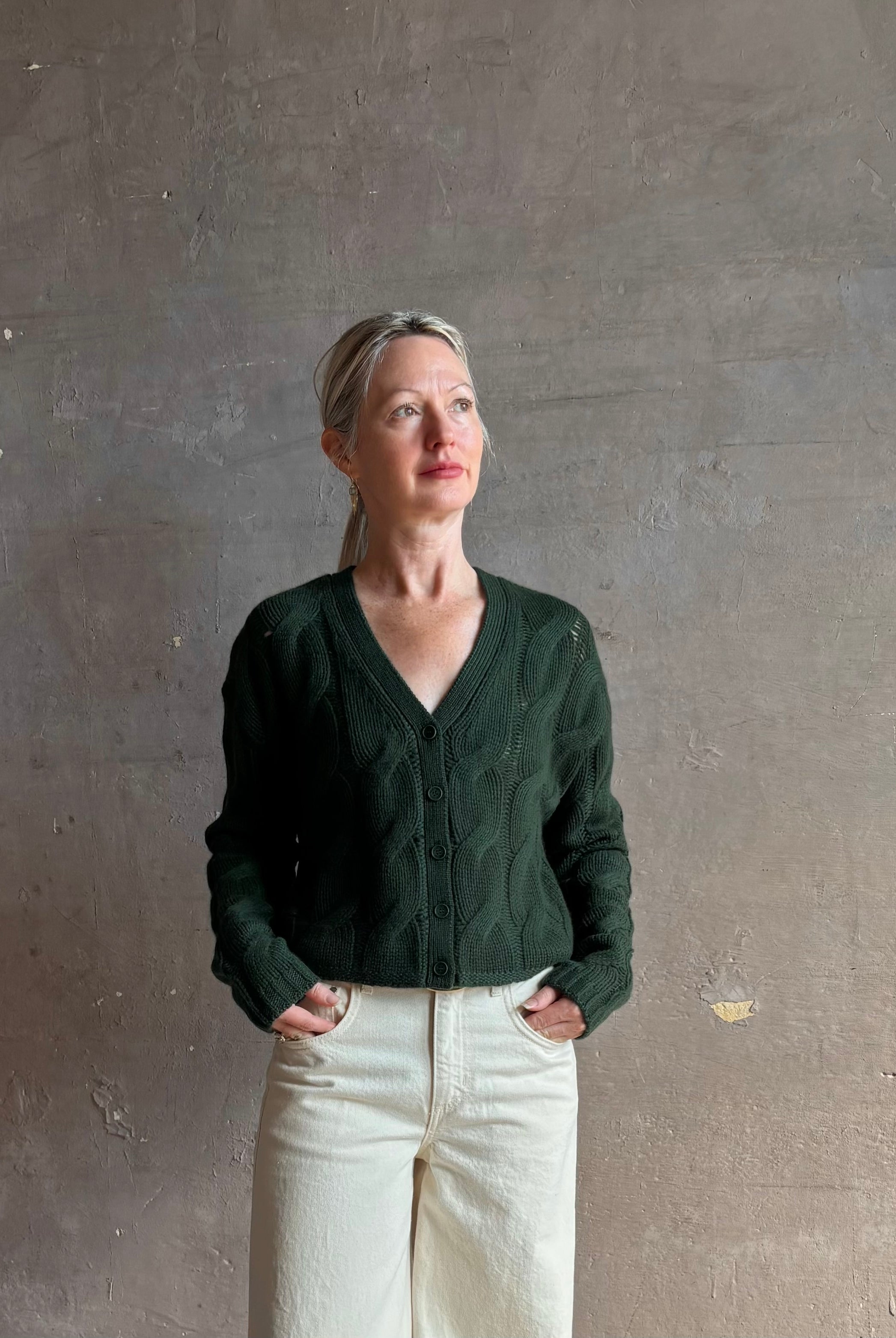 Mature woman wearing Sablyn Jolie dark green V-neck cropped cable-knit long sleeve cashmere cardigan sweater