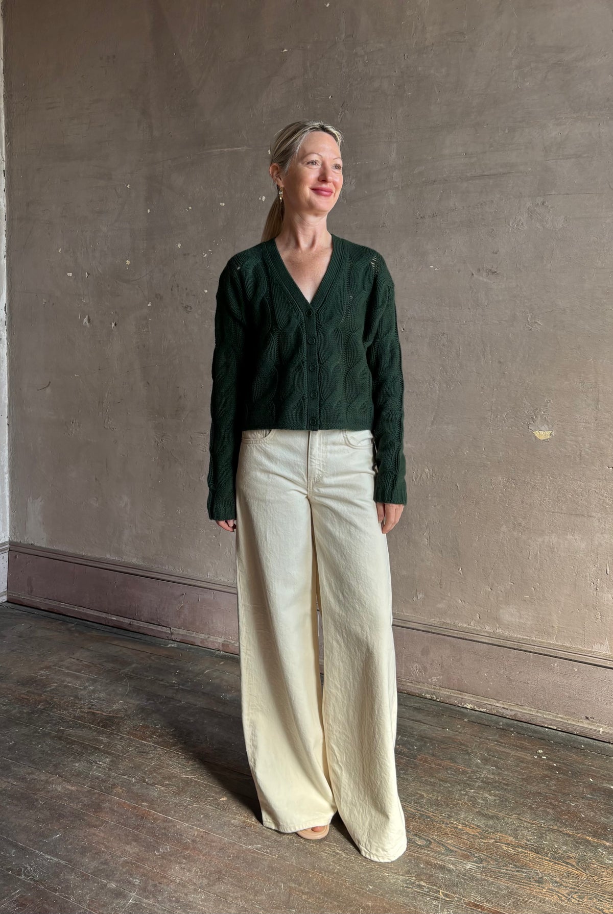 Mature woman wearing Sablyn Jolie dark green V-neck cropped cable-knit long sleeve cashmere cardigan sweater