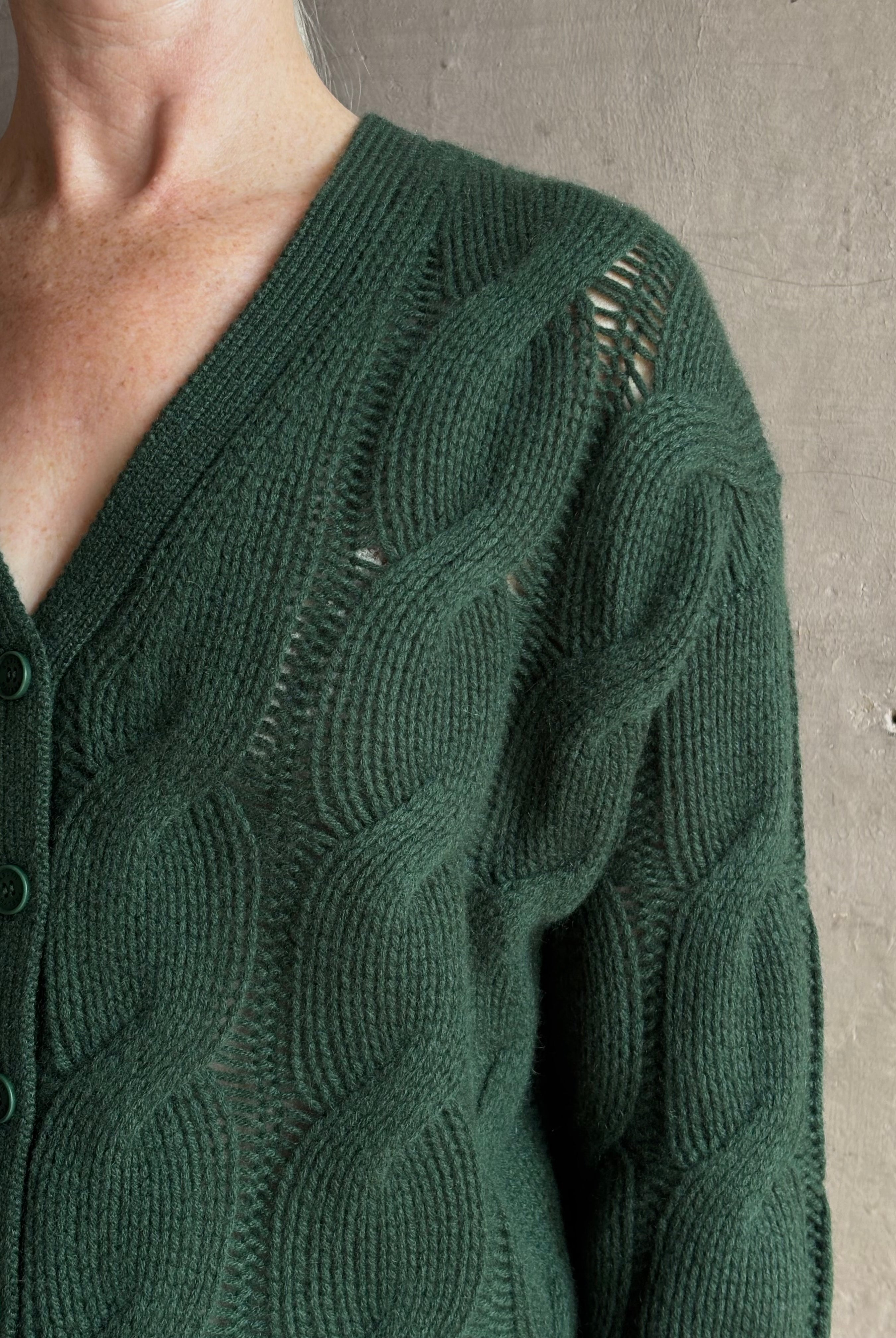 Mature woman wearing Sablyn Jolie dark green V-neck cropped cable-knit button front long sleeve cardigan