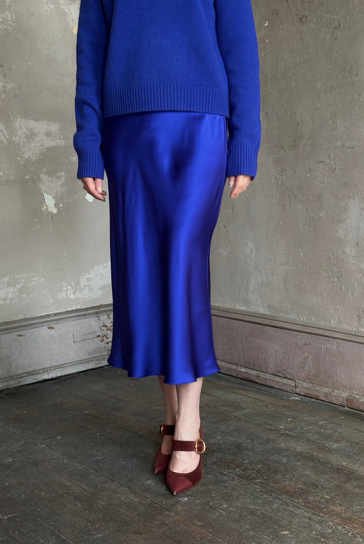 Mature woman wearing a vibrant royal blue silk bias cut midi skirt and matching cashmere knit sweater set
