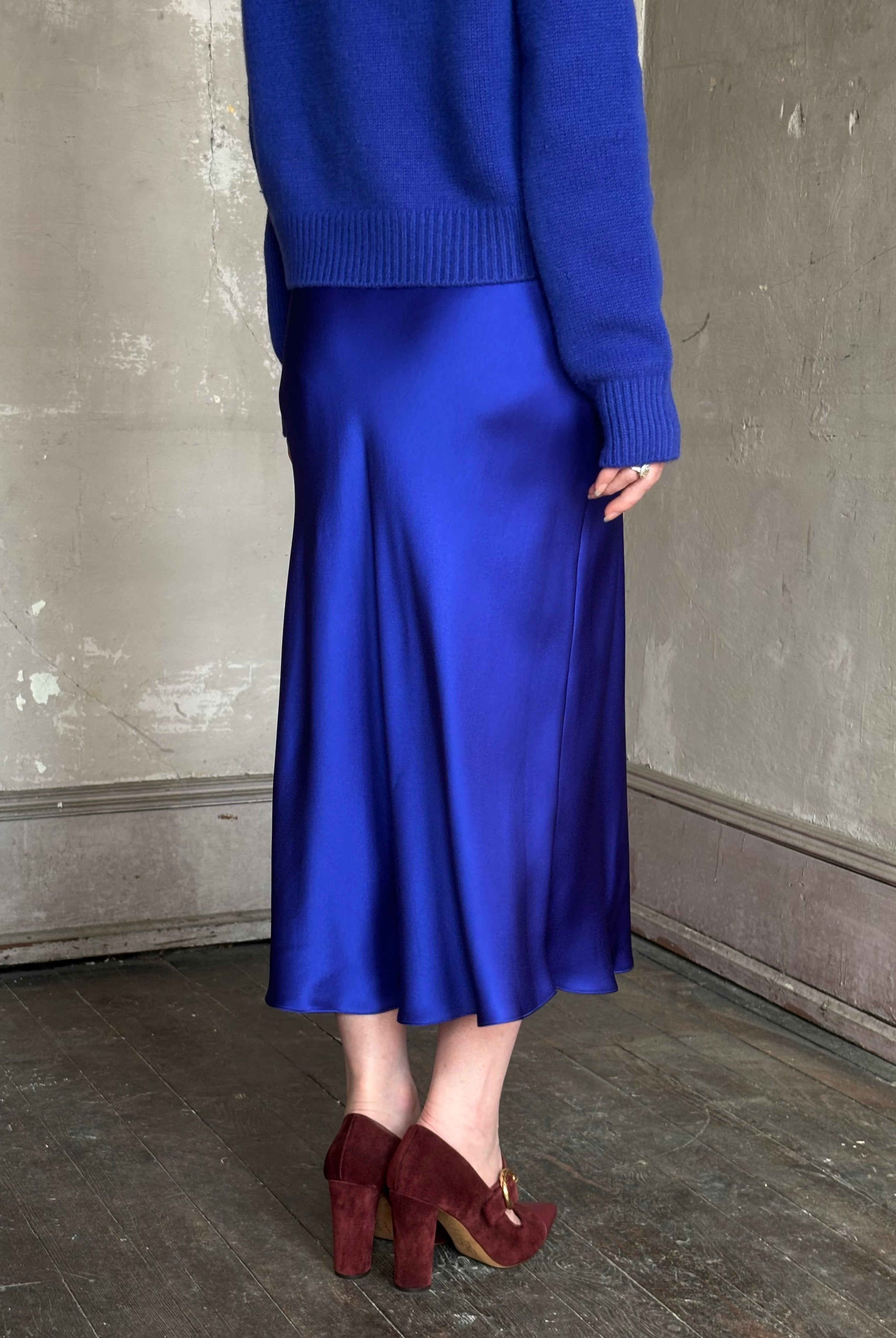 Mature woman wearing a vibrant royal blue silk bias cut midi skirt and matching cashmere knit sweater set