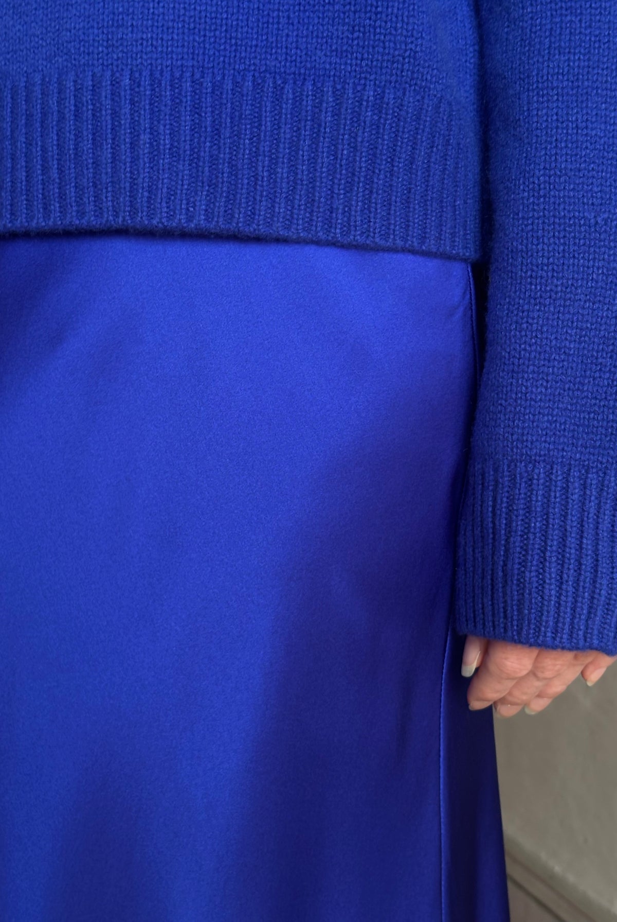Mature woman wearing a vibrant royal blue silk bias cut midi skirt and matching cashmere knit sweater set