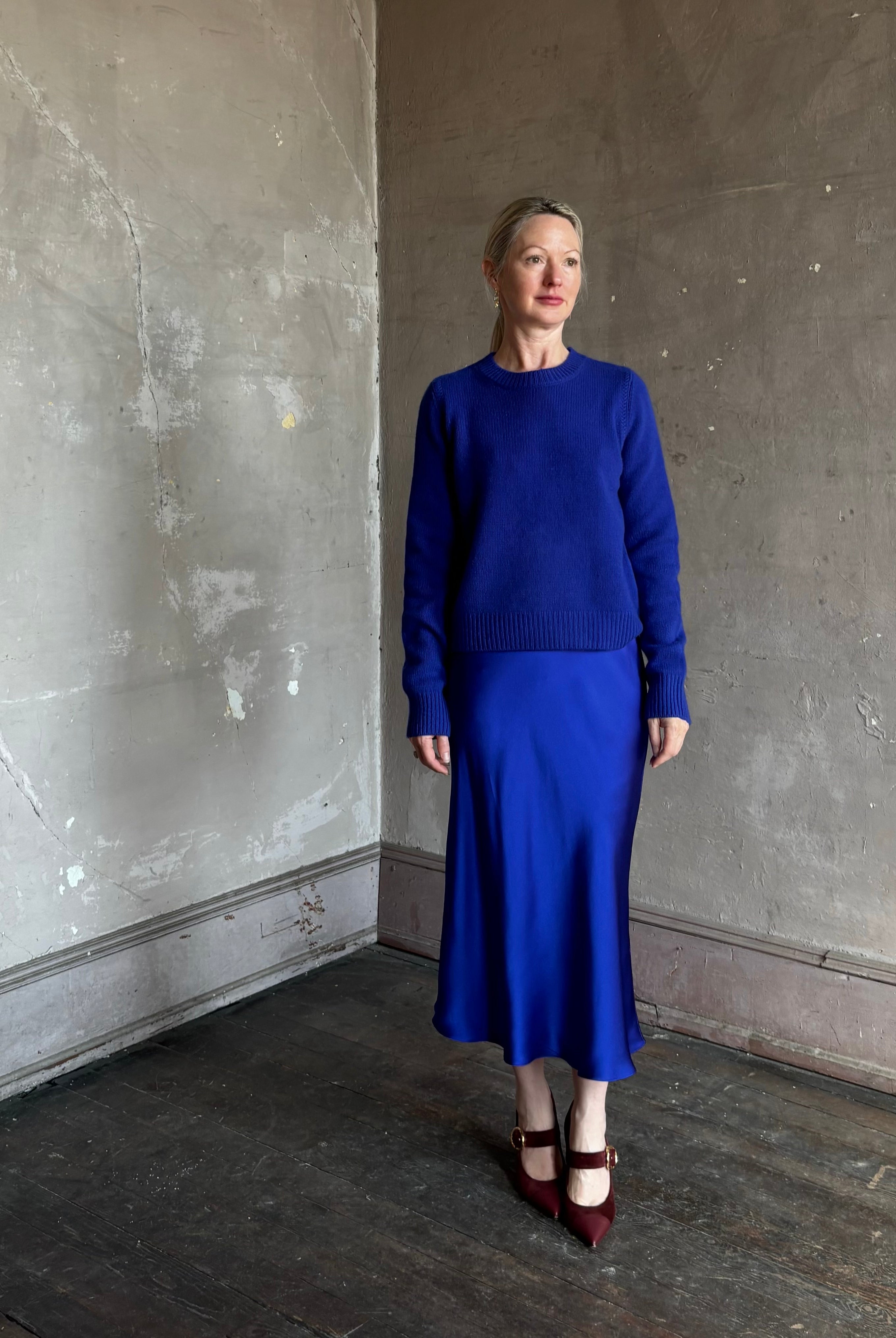 Mature woman wearing a vibrant royal blue silk bias cut midi skirt and matching cashmere knit sweater set