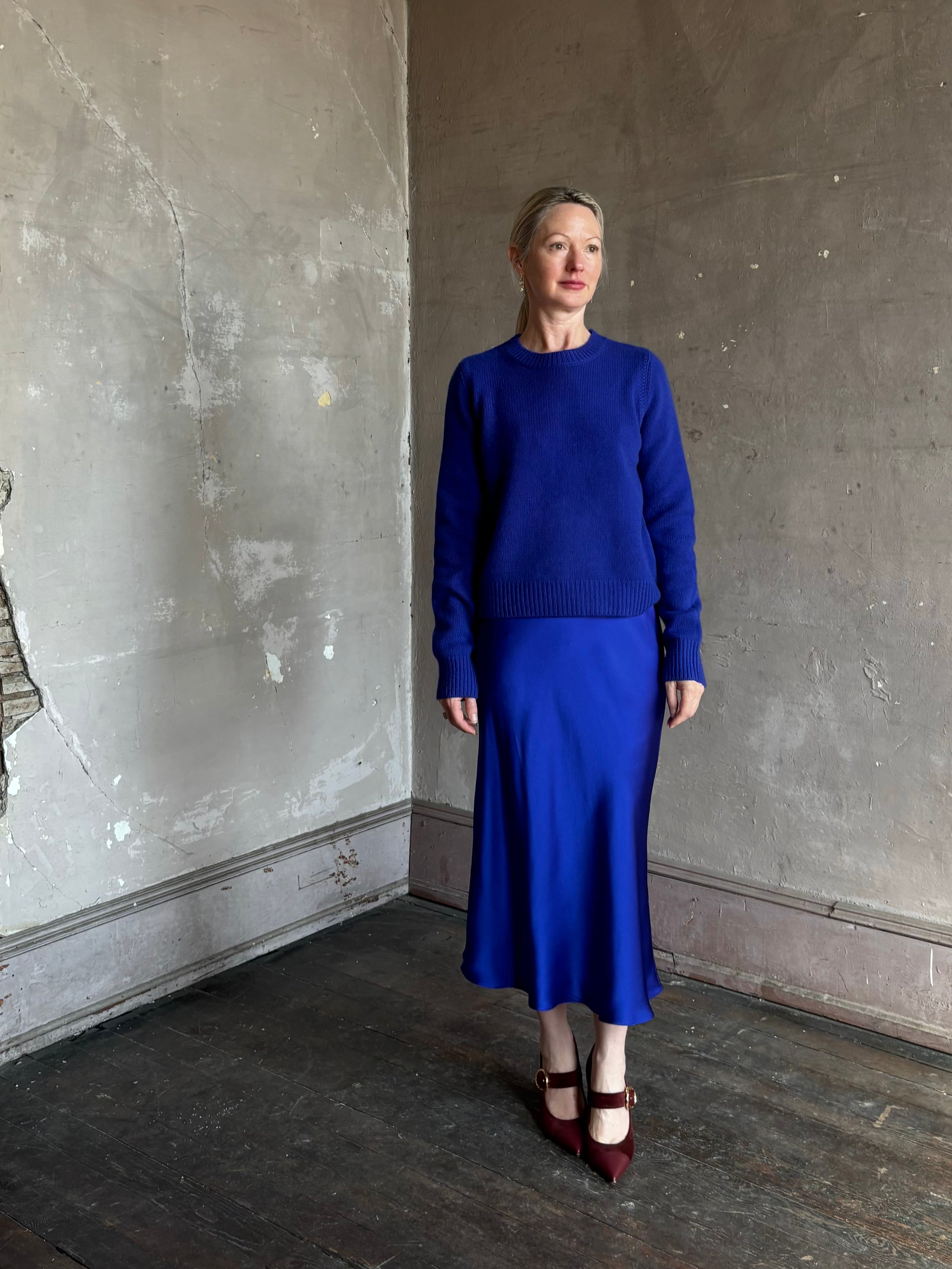 Mature woman wearing a vibrant royal blue silk bias cut midi skirt and matching cashmere knit sweater set