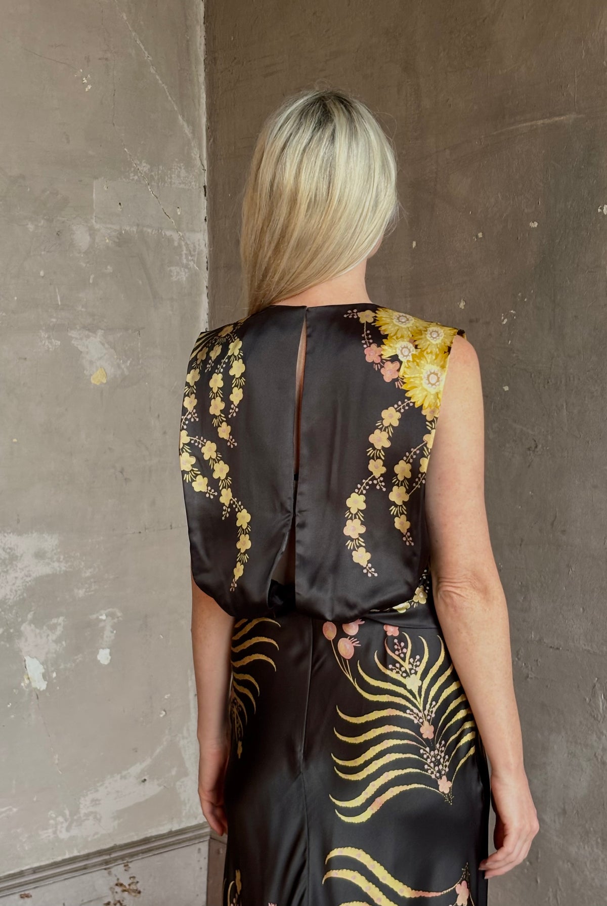Mature woman wearing Saloni Gwen Dress in Golden Palm semi-open back gathered waist black with yellow and pink print evening gown