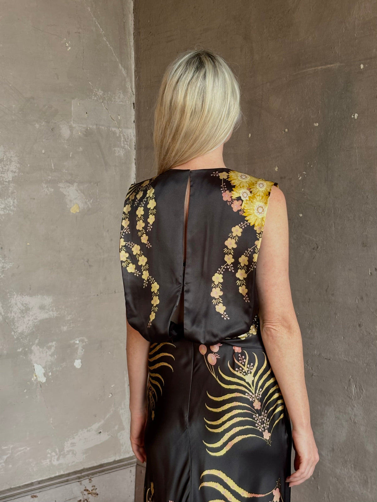 Mature woman wearing Saloni Gwen Dress in Golden Palm semi-open back gathered waist black with yellow and pink print evening gown